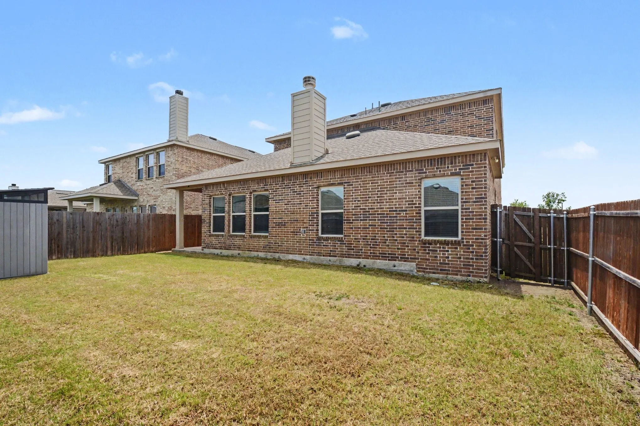 Spacious backyard featuring a brick exterior, covered patio, fenced perimeter, and a detached storage shed