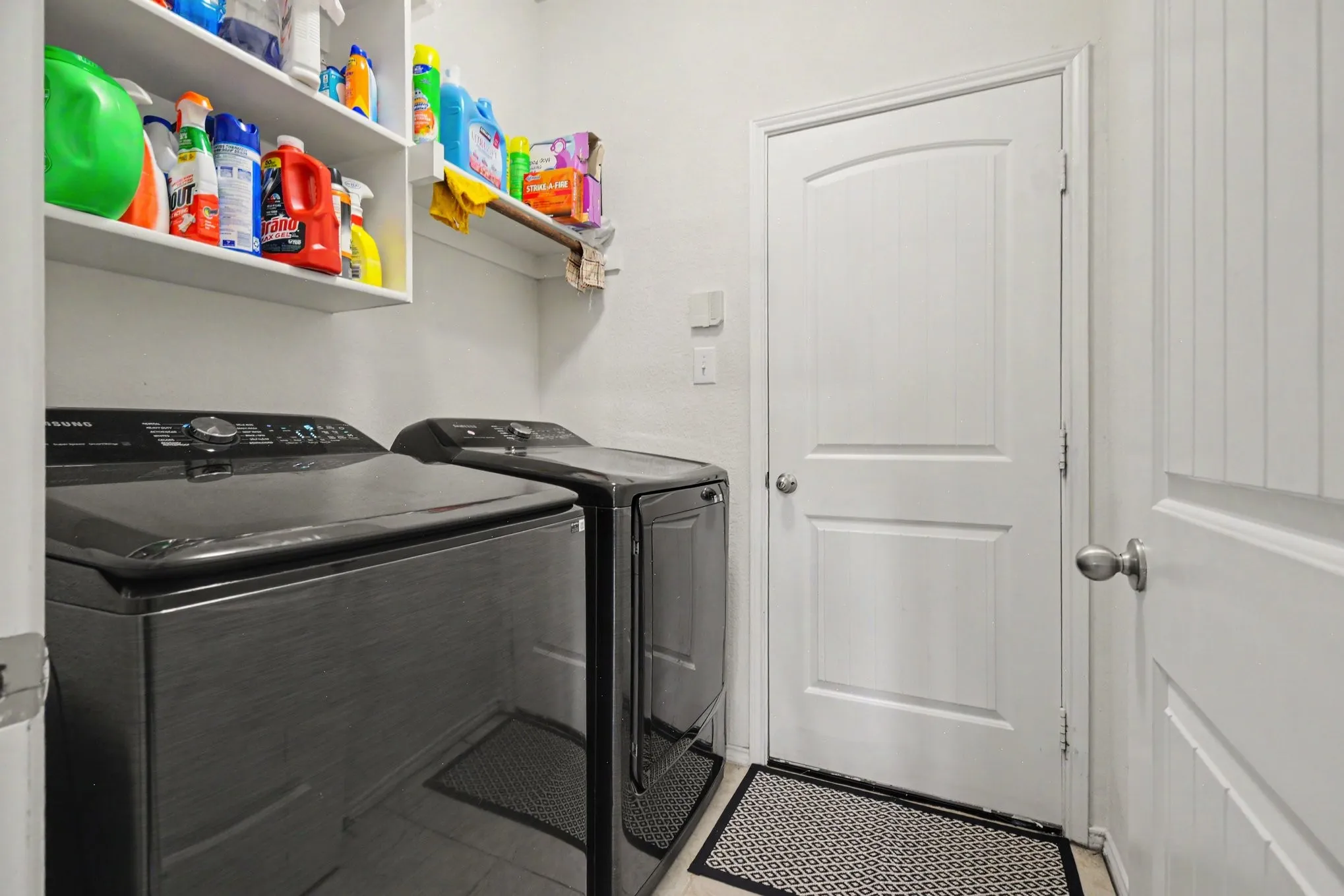 Dedicated utility space featuring built-in white shelving, light-colored flooring, and a white paneled door with an arched top detail