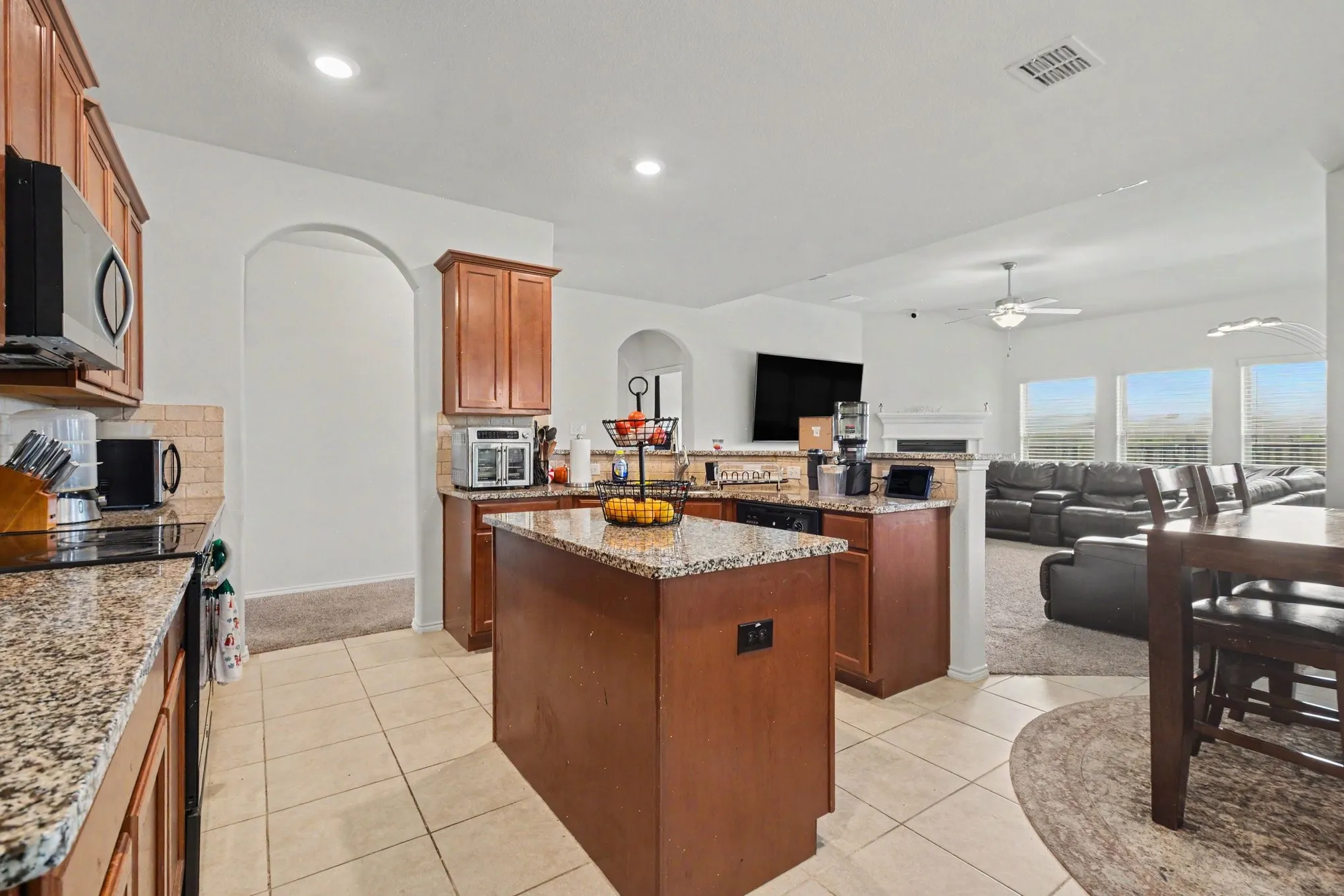 Kitchen featuring a central island with a granite-style countertop, tile flooring, wood cabinetry, stainless steel appliances, and a tiled backsplash
