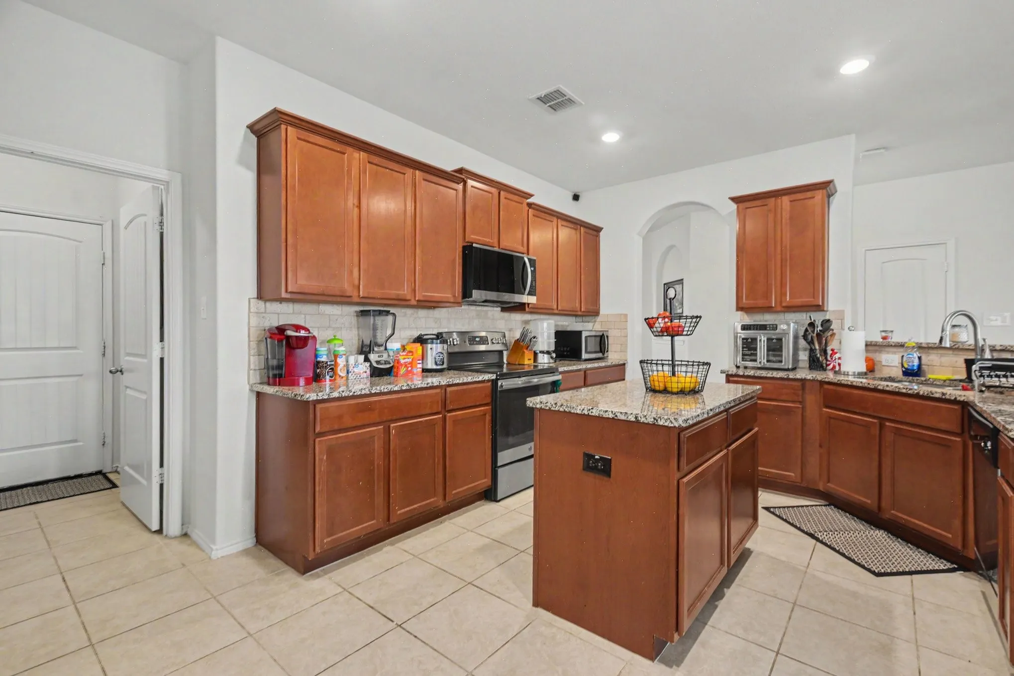 Kitchen featuring wood cabinetry, granite countertops, tile flooring, a tile backsplash, and a built-in microwave