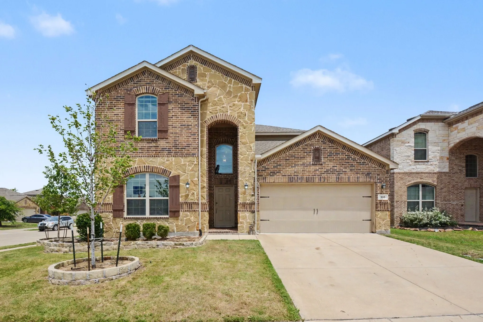 Two-story residence featuring a brick and stone facade, arched windows with shutters, an arched entryway, an attached garage, and a concrete driveway