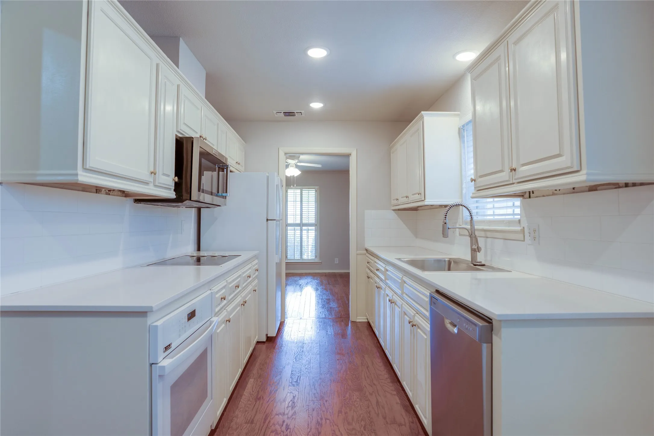 Galley kitchen featuring white cabinetry, light-toned countertops, and a white subway tile backsplash