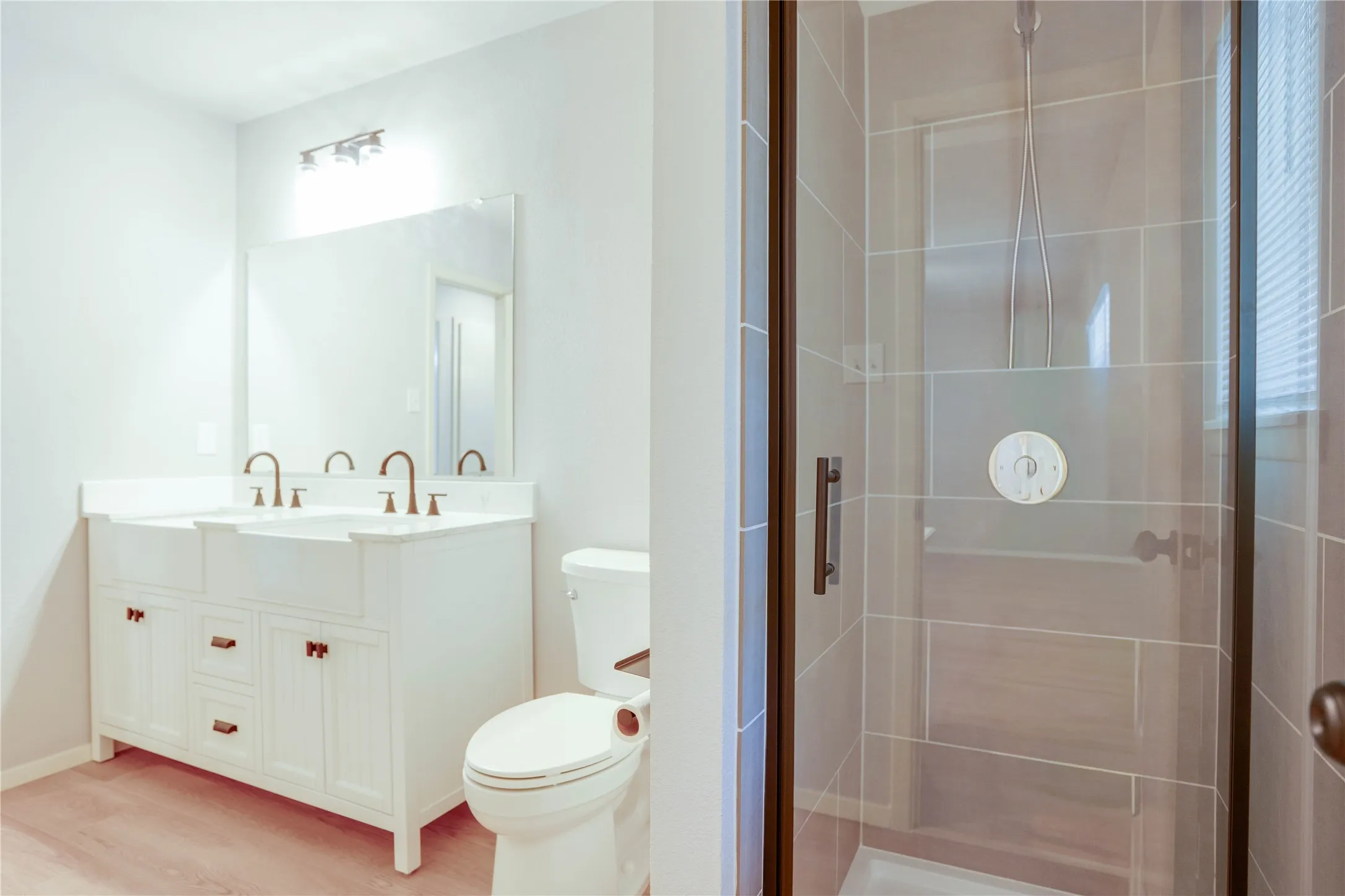 Bathroom featuring a double vanity with farmhouse sinks, quartz-finish countertop, dark bronze fixtures, and a glass-enclosed shower with tiled walls
