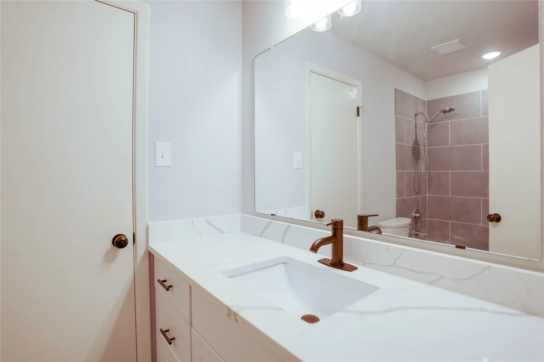 Vanity featuring a white countertop with subtle veining, integrated rectangular sink, and a bronze-finish faucet