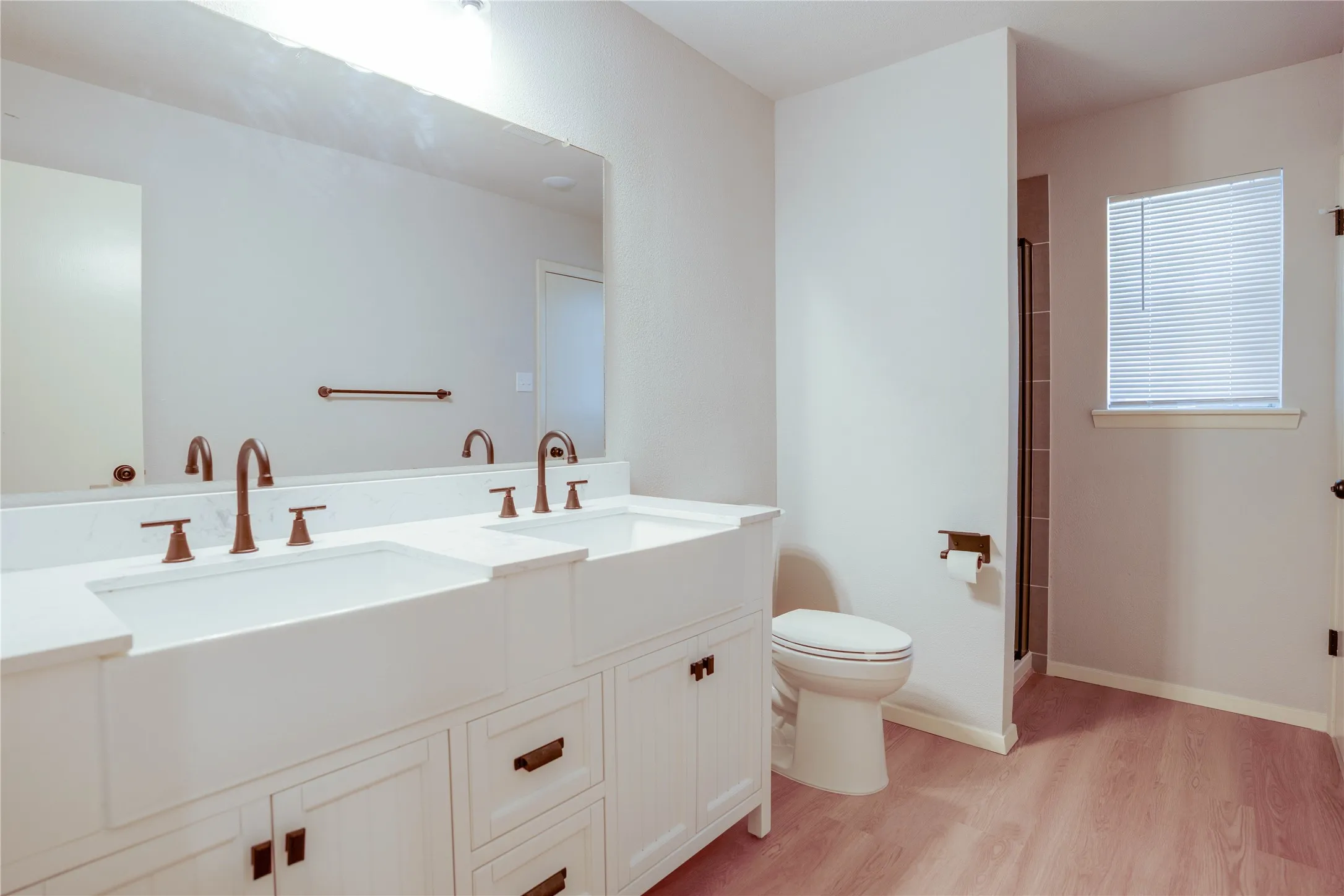 Double vanity with white apron-front sinks, bronze-finish fixtures, and a light-toned countertop