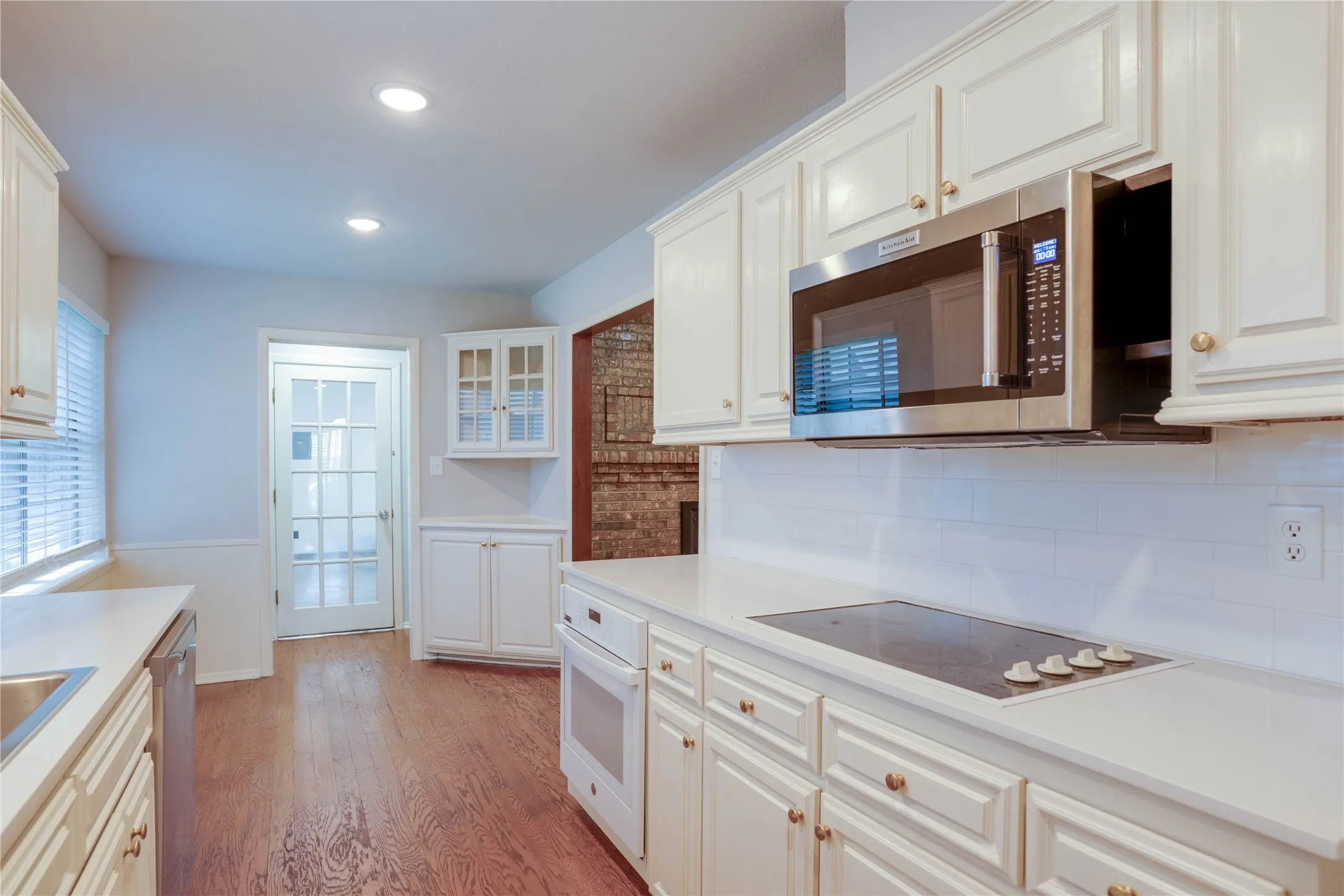 Kitchen featuring white cabinetry with gold-toned hardware, solid surface countertops, and hardwood flooring