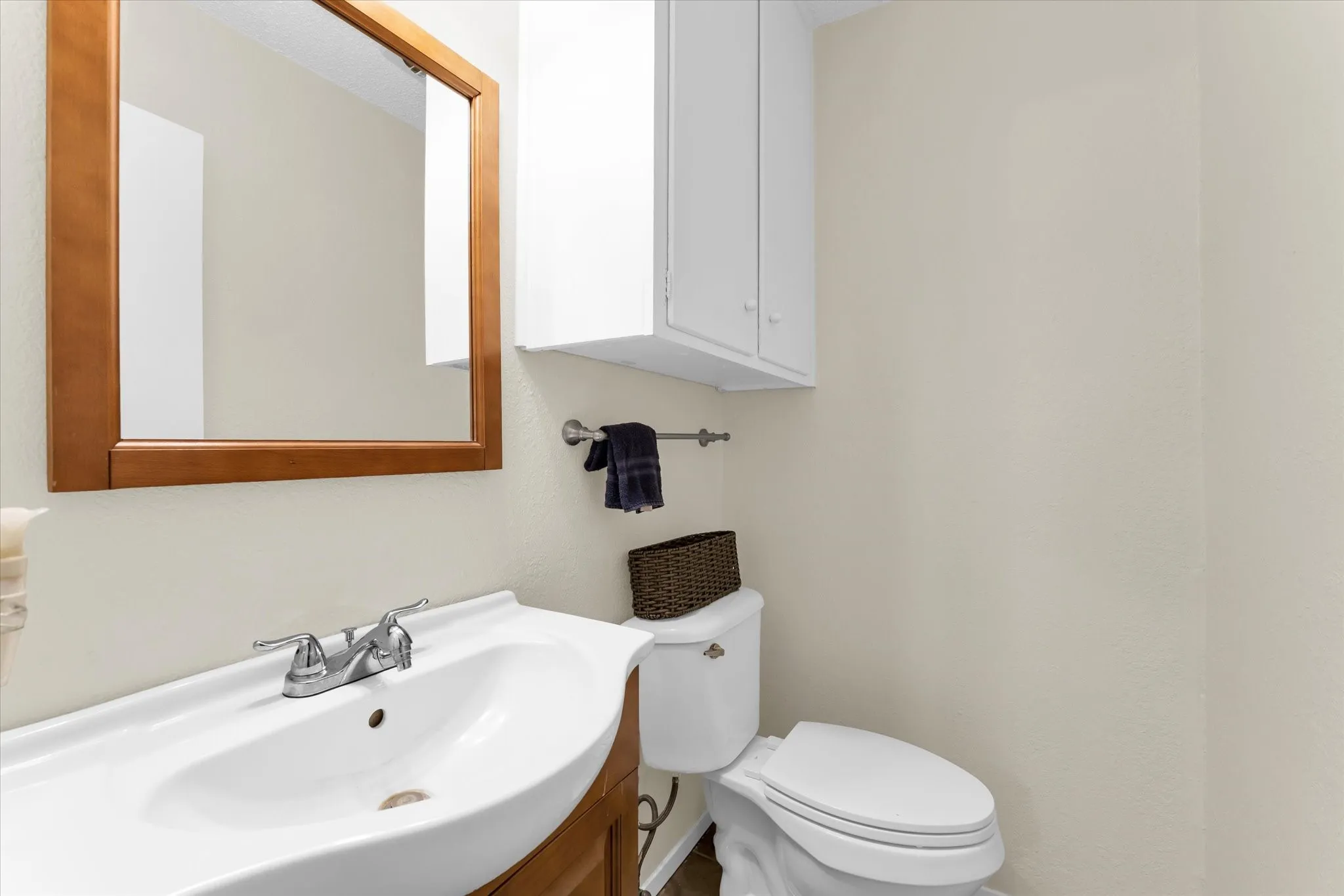 Bathroom vanity featuring a white porcelain sink with chrome faucet, a wood-framed mirror, and a white toilet