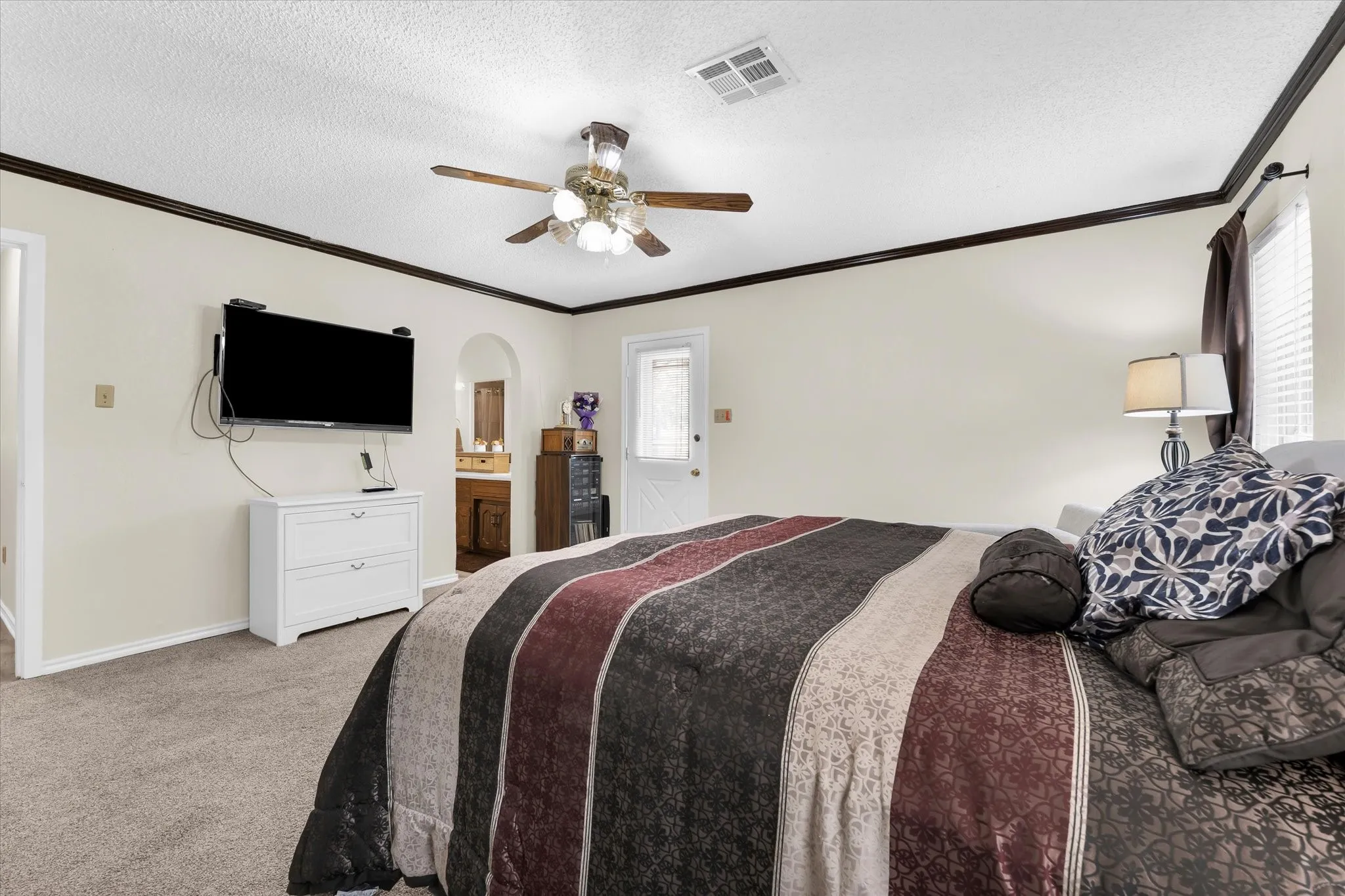 Carpeted room featuring a ceiling fan with integrated lighting, dark crown molding, and a white paneled door