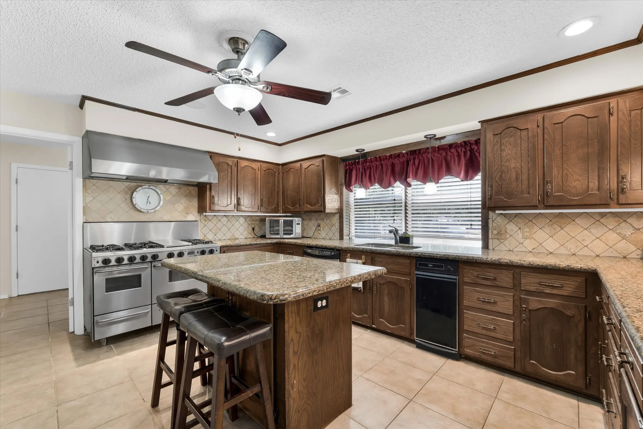 Kitchen featuring an oversized stainless steel range with a professional-grade hood, wood cabinetry, granite countertops, and tile flooring