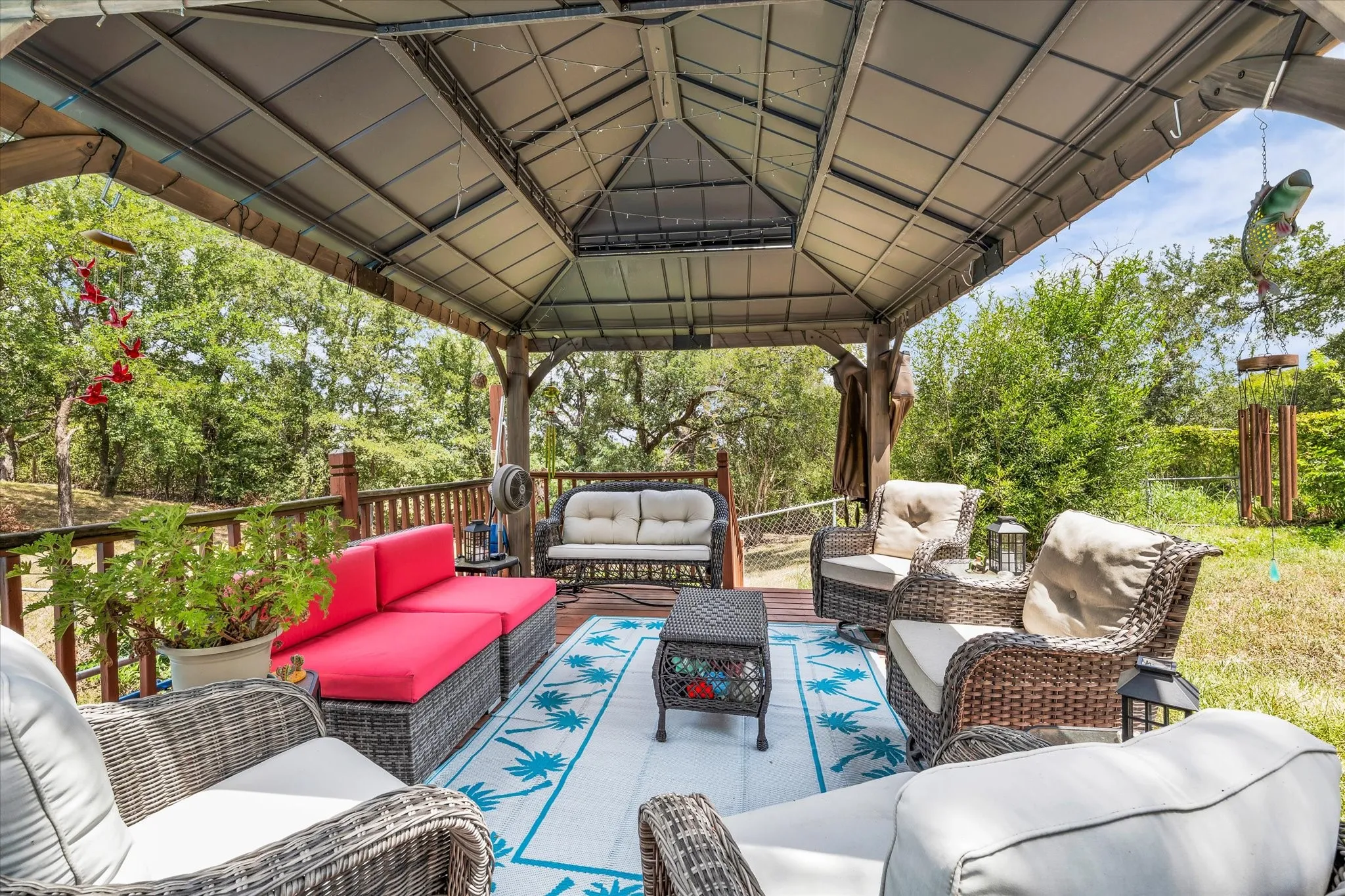 Covered outdoor patio featuring a metal gazebo structure, wood deck, and surrounding greenery