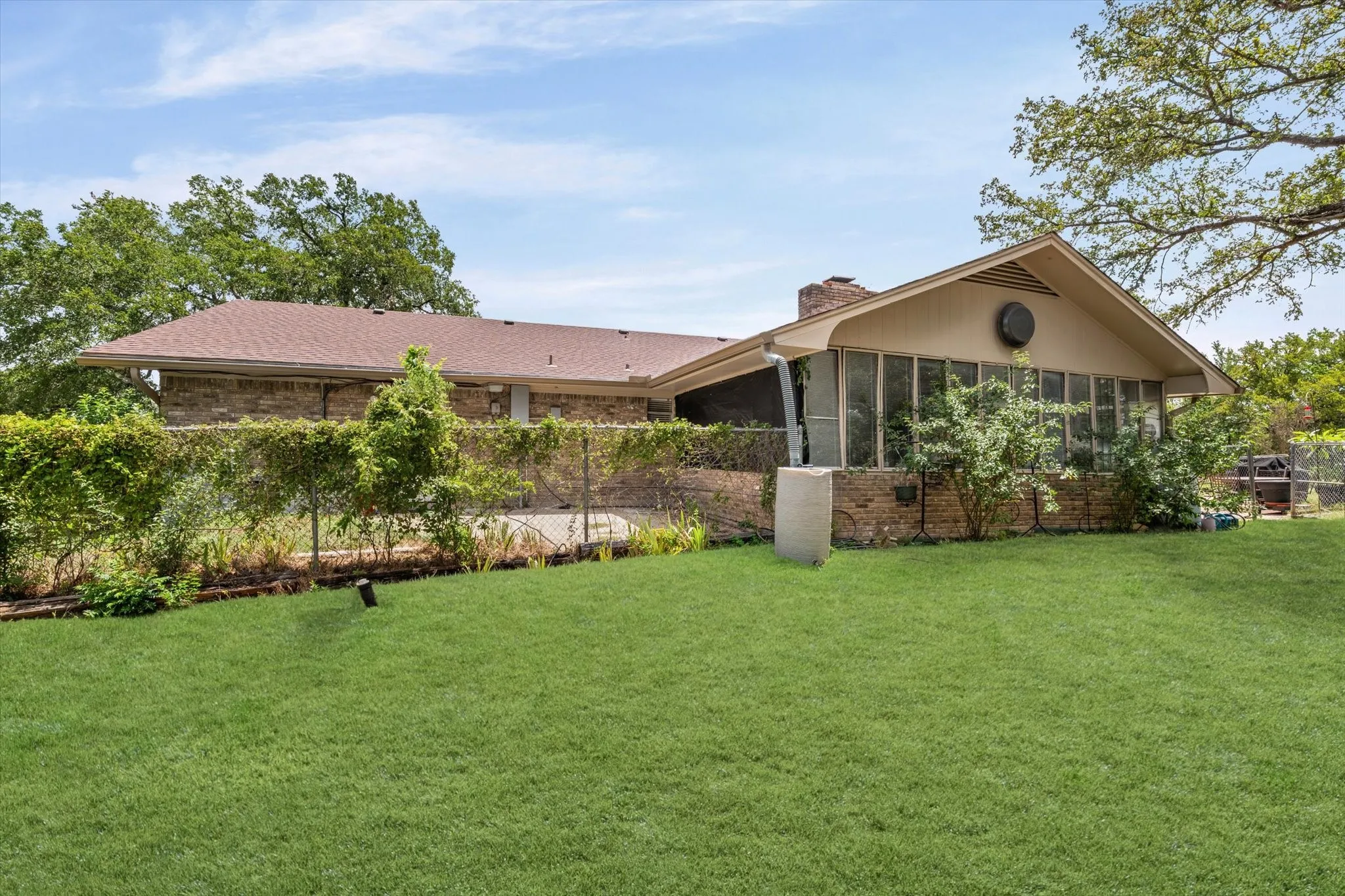 Expansive backyard featuring a green lawn, mature trees, and a brick exterior home with a screened-in porch