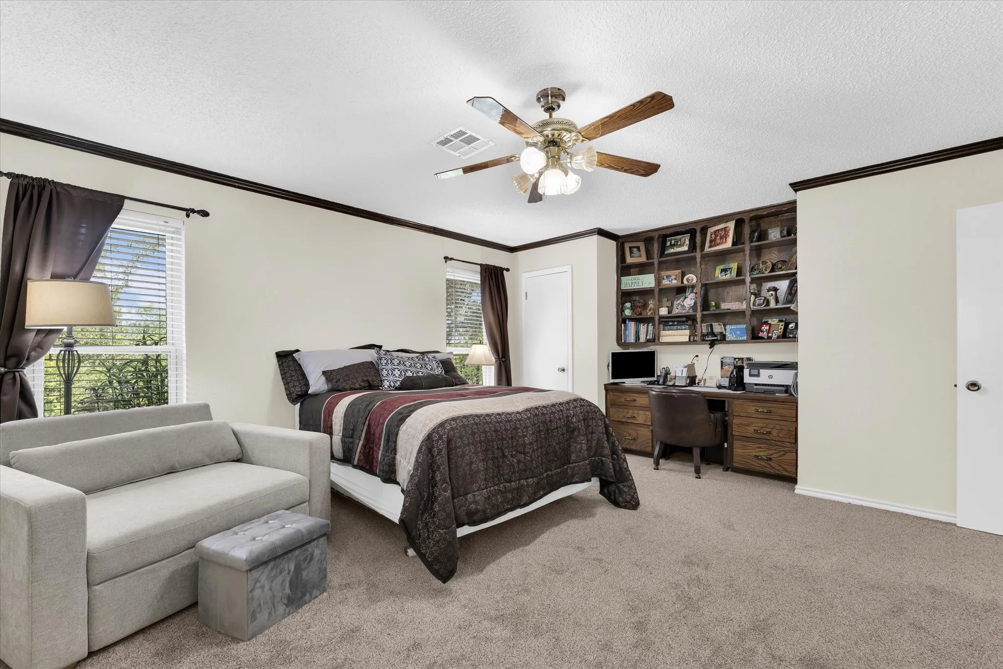 Carpeted bedroom featuring built-in wood cabinetry, integrated desk space, and a ceiling fan with light fixture