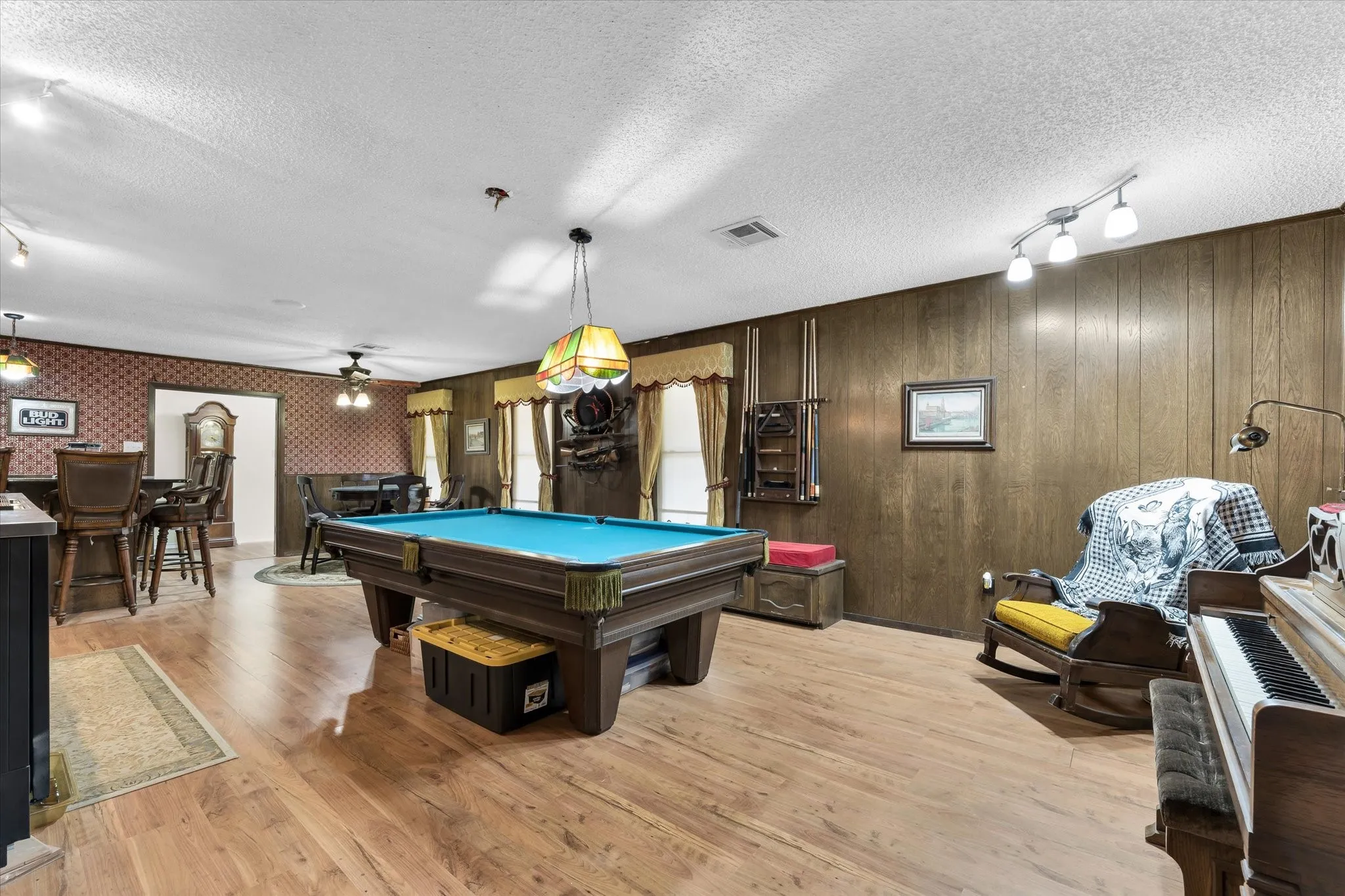 Spacious room featuring wood-finish flooring, wood-paneled accent wall, and a dropped acoustic panel ceiling