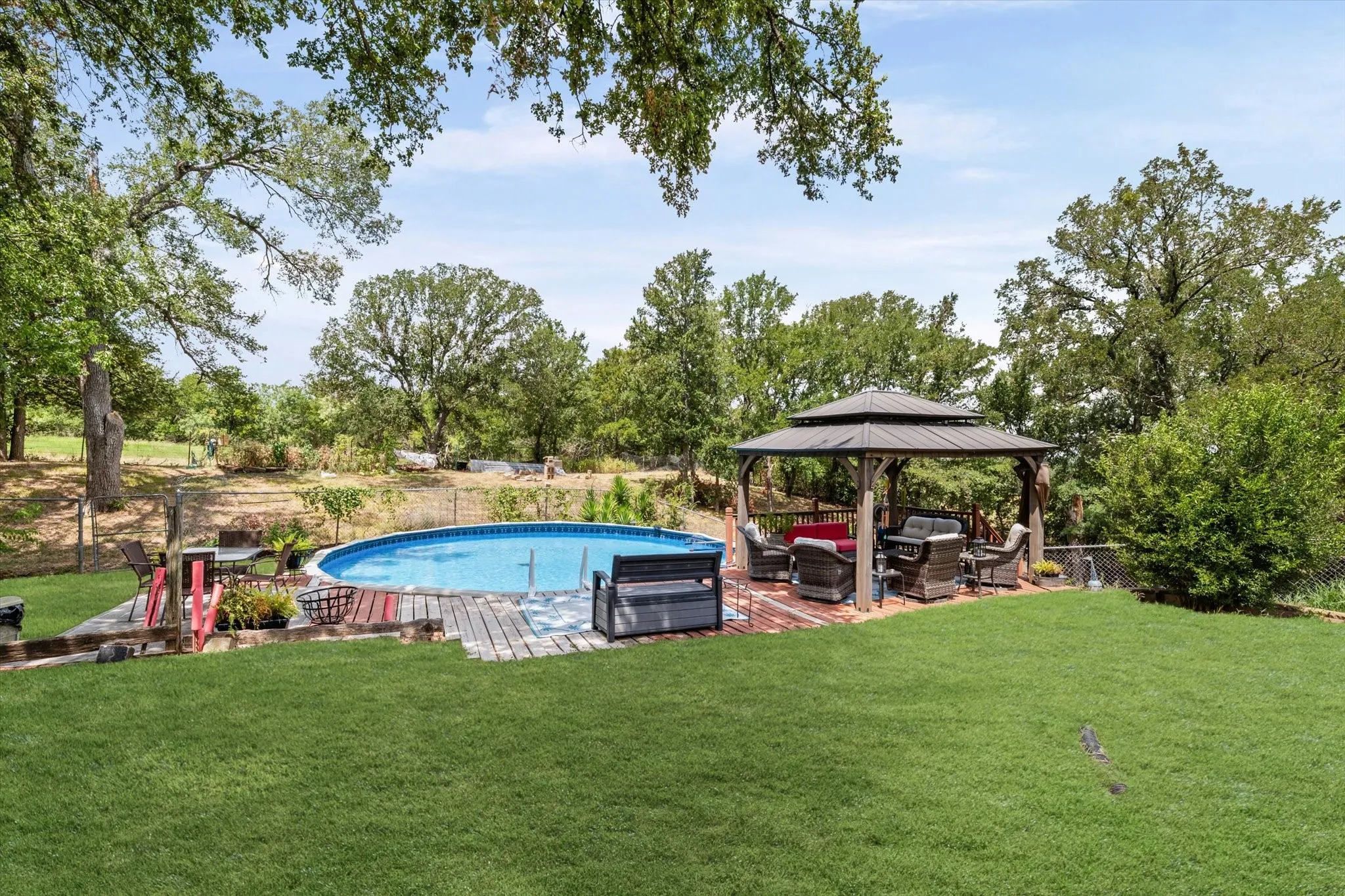 Expansive backyard featuring a circular above-ground pool, a wooden deck surround, and a covered gazebo