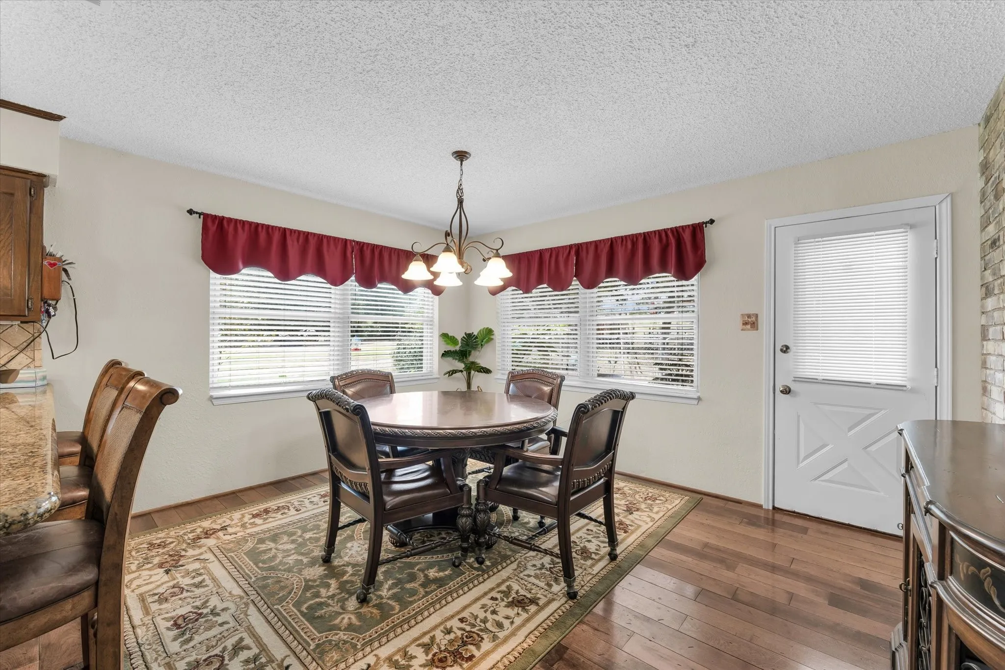 Dining area featuring wood-finish flooring, two large windows with blinds, and a white exterior door with integrated blinds