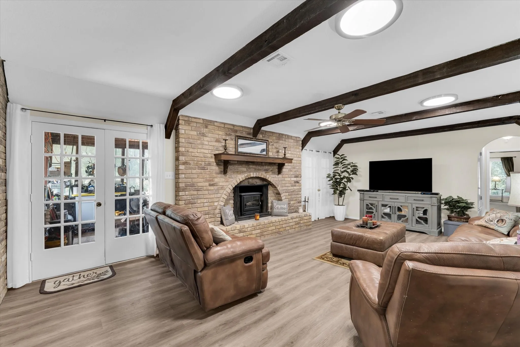 Living area featuring exposed ceiling beams, wood-finish flooring, and a brick fireplace with a wood mantle