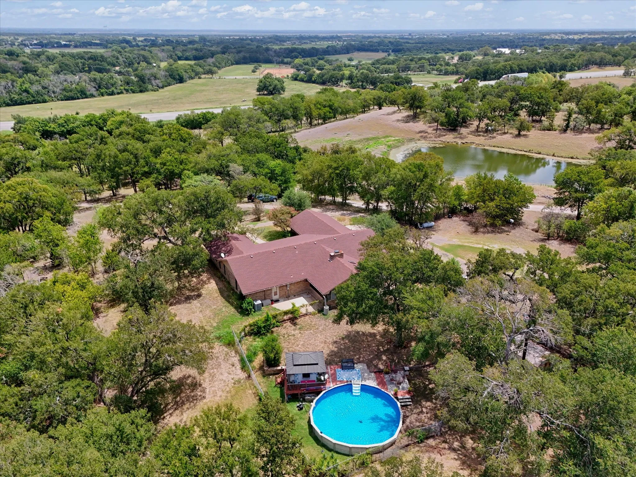 Expansive property featuring a single-story residence with a red tile roof, surrounded by mature trees