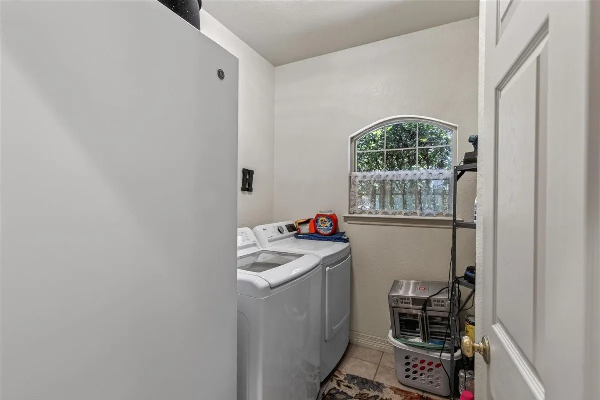 Launder room with washer-dryer connection, featuring light beige walls, a tiled floor, arched window, and room for an extra freezer