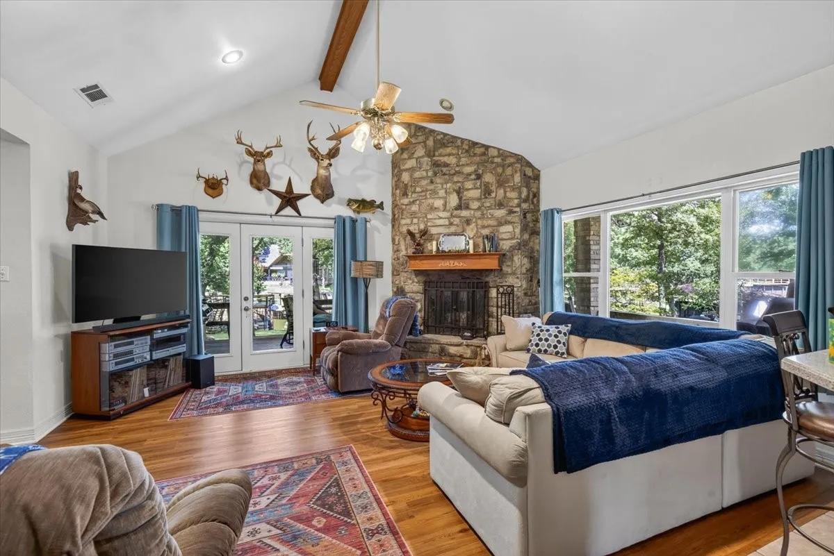 Spacious living area featuring a vaulted ceiling with exposed wood beams, luxury vinyl plank flooring, and a stone-clad fireplace with a wo