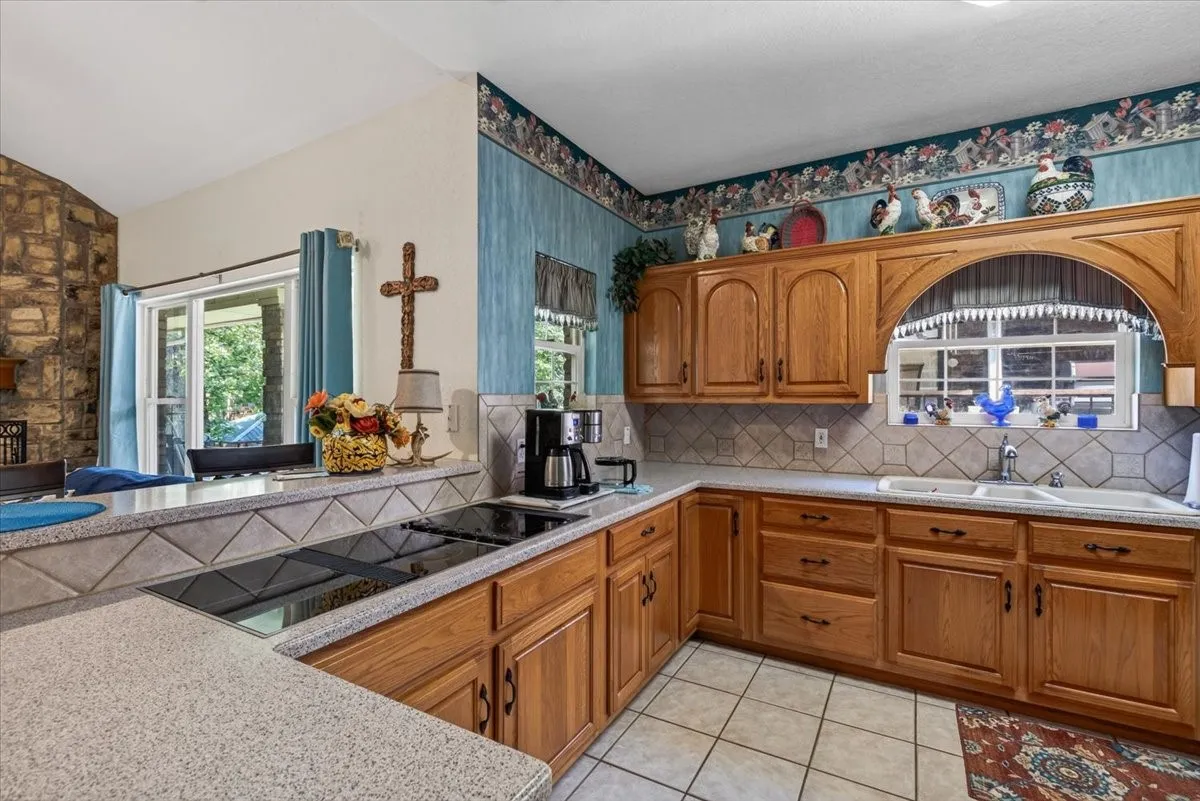 Kitchen featuring wood cabinetry, solid surface countertops, a Jenn-Aire downdraft cooktop, and a tile backsplash