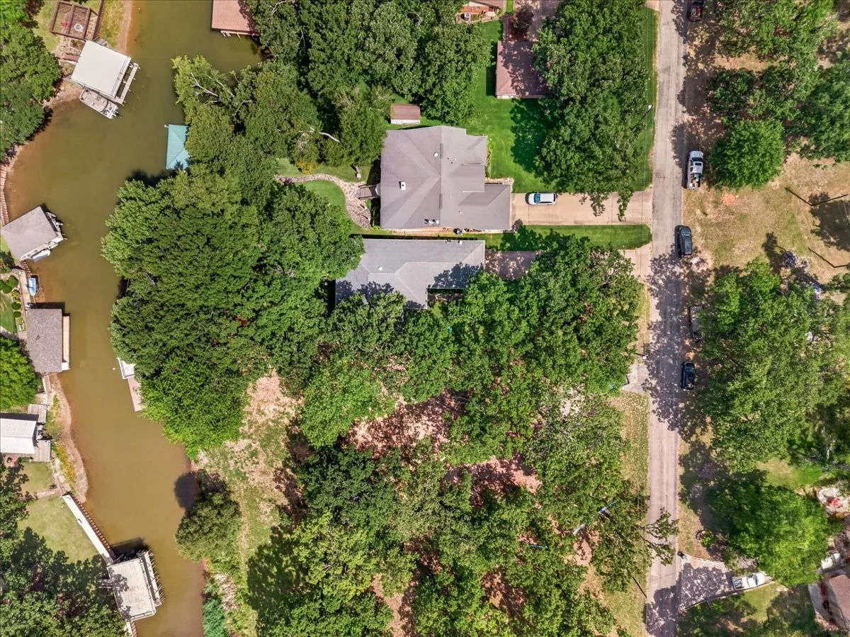 Waterfront property featuring a private boat dock, mature tree coverage, a dedicated driveway, a residential street frontage, and waterfront channel