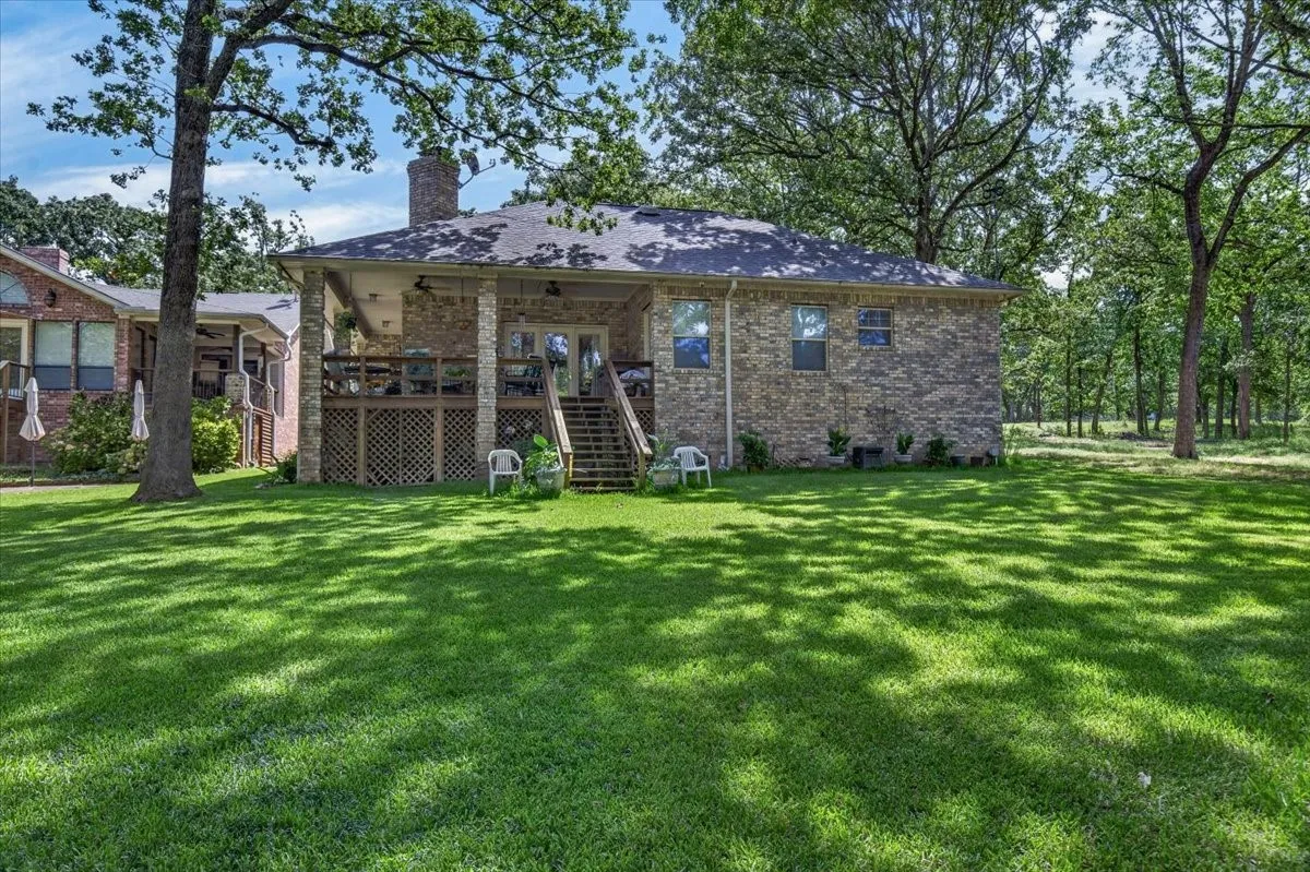 Expansive lakeside yard featuring a manicured lawn, mature trees, and a large covered porch.  Sit a spell and enjoy watching friends and family playing yard games and those fishing and swimming.