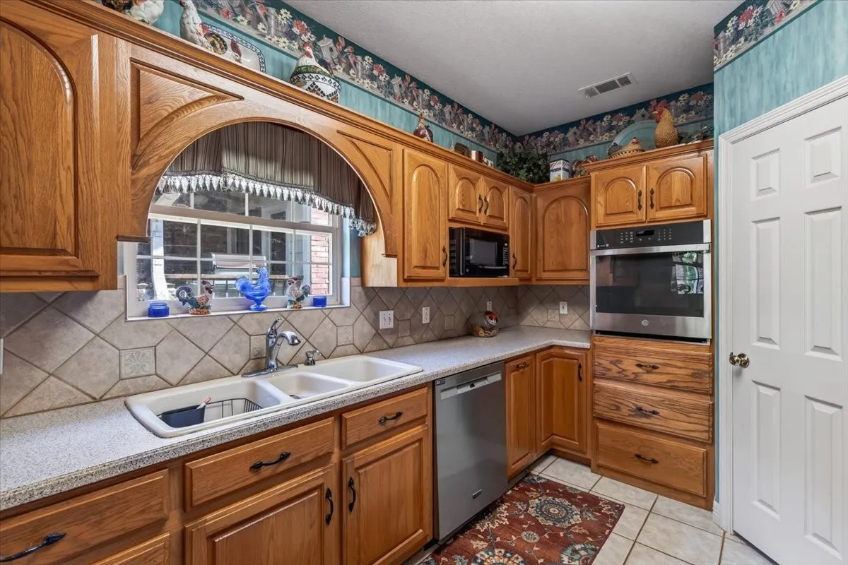 Kitchen featuring wood cabinetry, A triple-bowl sink, a stainless steel dishwasher, a built-in stainless steel oven, and walk-in pantry.
