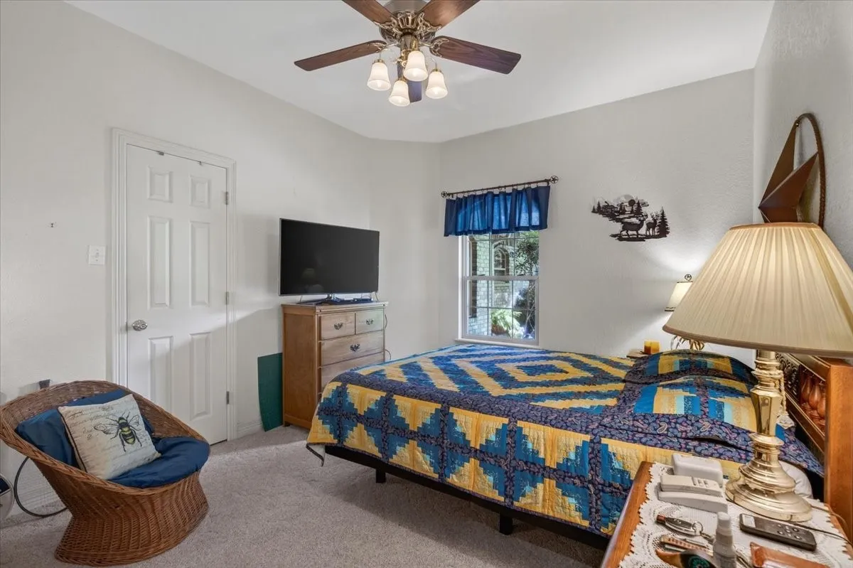 Carpeted bedroom featuring a ceiling fan with light fixture, a window with blue valance, and a paneled door