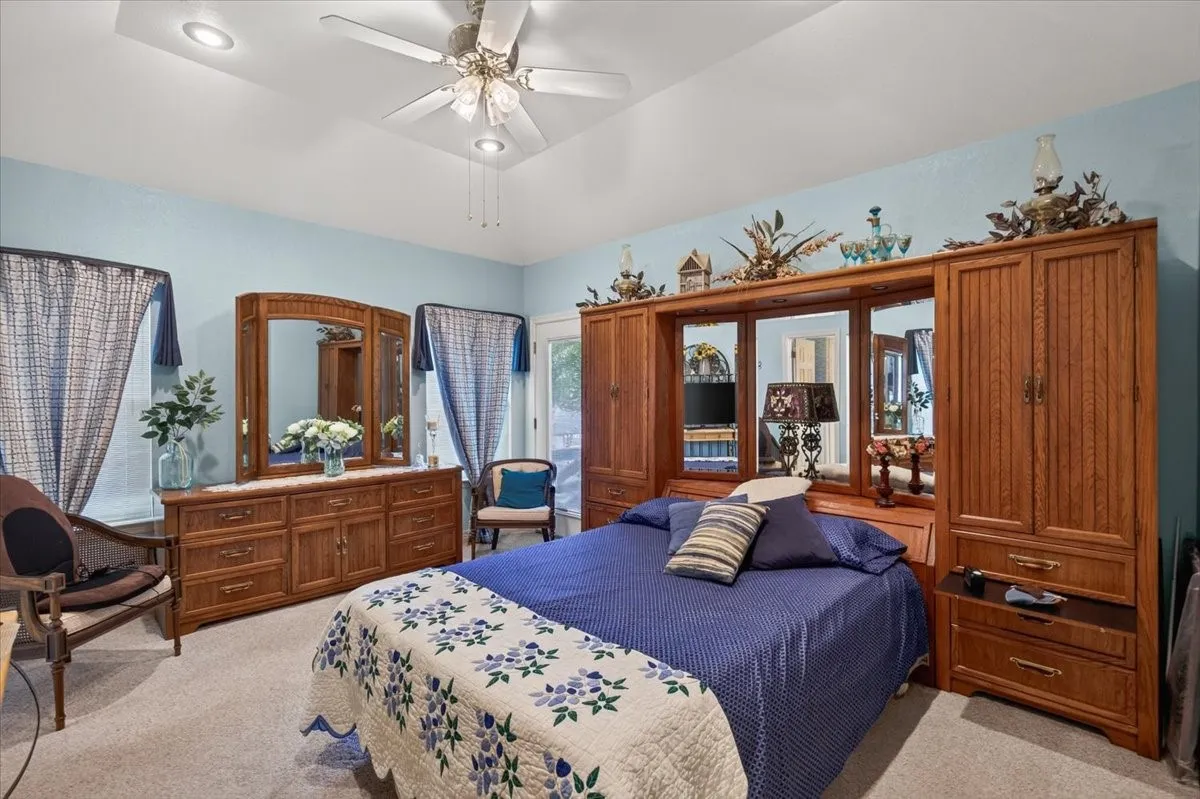 Tray ceiling with recessed lighting and a ceiling fan, wall-to-wall carpeting, and multiple windows with blinds, french door to lakeside porch.