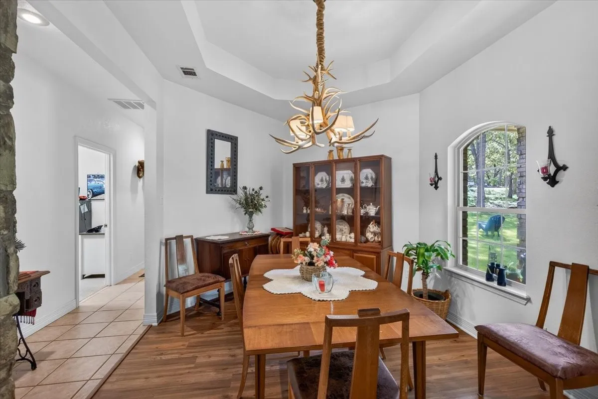 Dining space featuring vinyl luxury plank flooring, a tray ceiling, and an arched window (custom antler light is excluded).