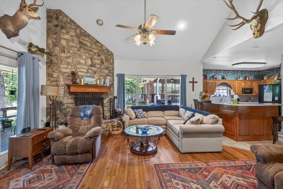 Spacious living area featuring a vaulted ceiling and a floor-to-ceiling stone fireplace with a wood mantle. Open floorplan