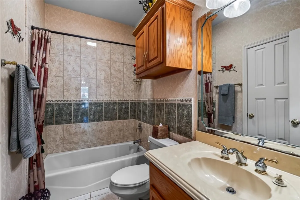 Bathroom featuring a tub-shower with tiled surround, a toilet, and a vanity with an integrated sink and wood cabinetry