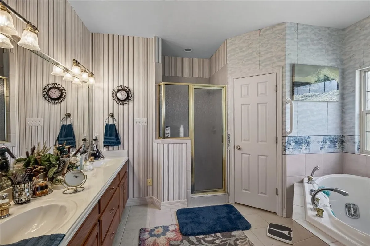 Bathroom featuring a dual vanity with a light-toned countertop, a built-in shower with a gold-toned frame, a jetted tub, and 2 separate walk-in closets