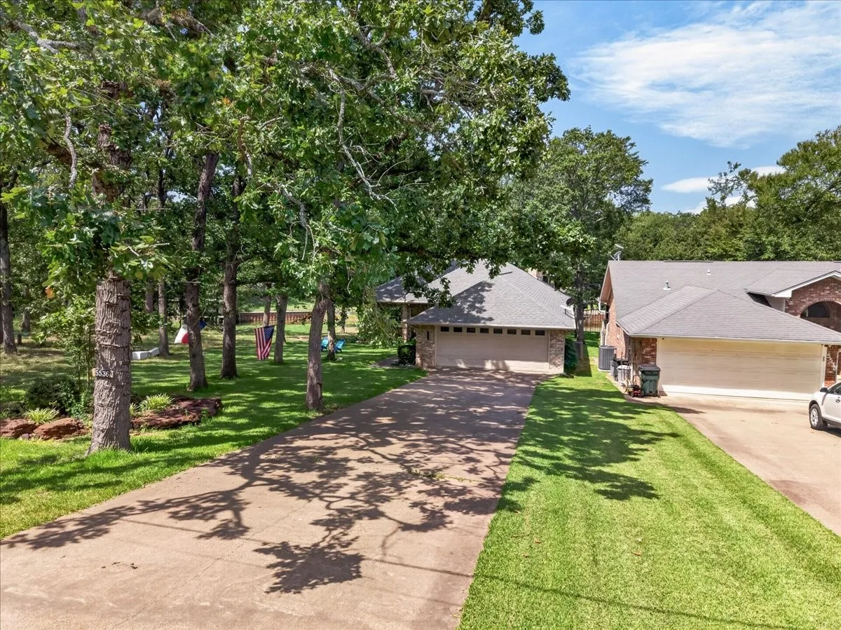 Paved driveway leading to a residence with an attached two-car garage, brick facade, and a shingle roof
