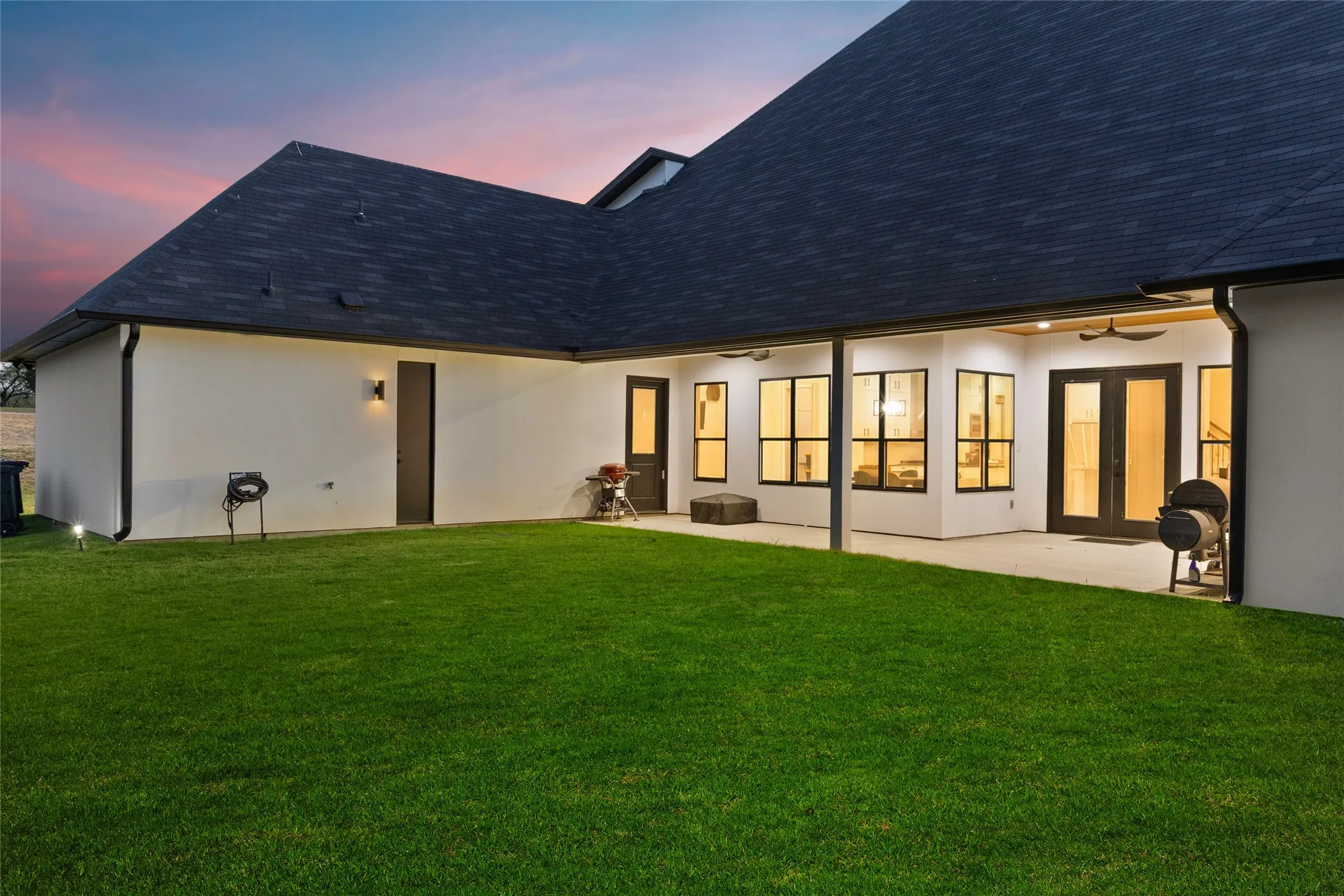 Expansive lawn area with a covered patio, multiple large windows, and a set of double doors providing exterior access