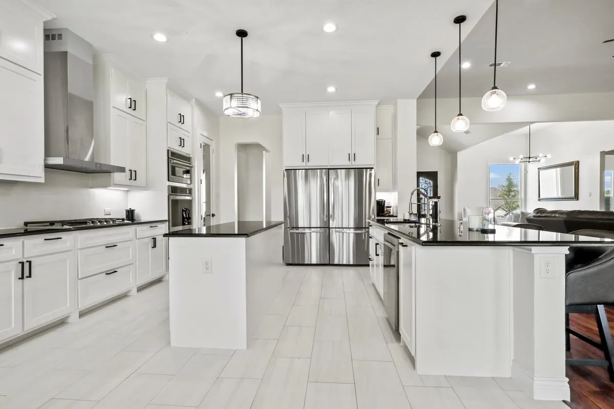 Kitchen featuring white cabinetry, black countertops, stainless steel appliances, and two central islands with pendant lighting