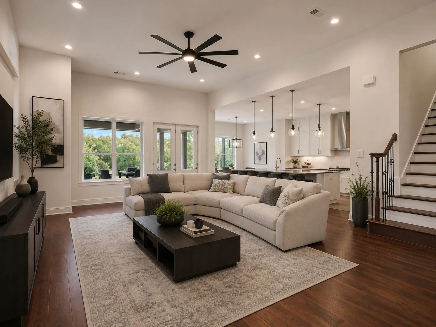 Spacious living area featuring rich wood-finish flooring, a modern black ceiling fan, and large windows with transom details