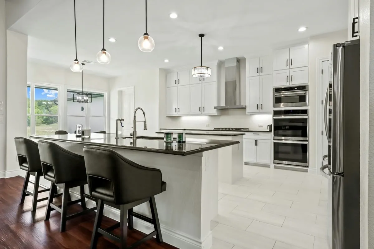 White cabinetry, dark stone countertops, stainless steel appliances, recessed lighting, and a large center island with pendant lighting
