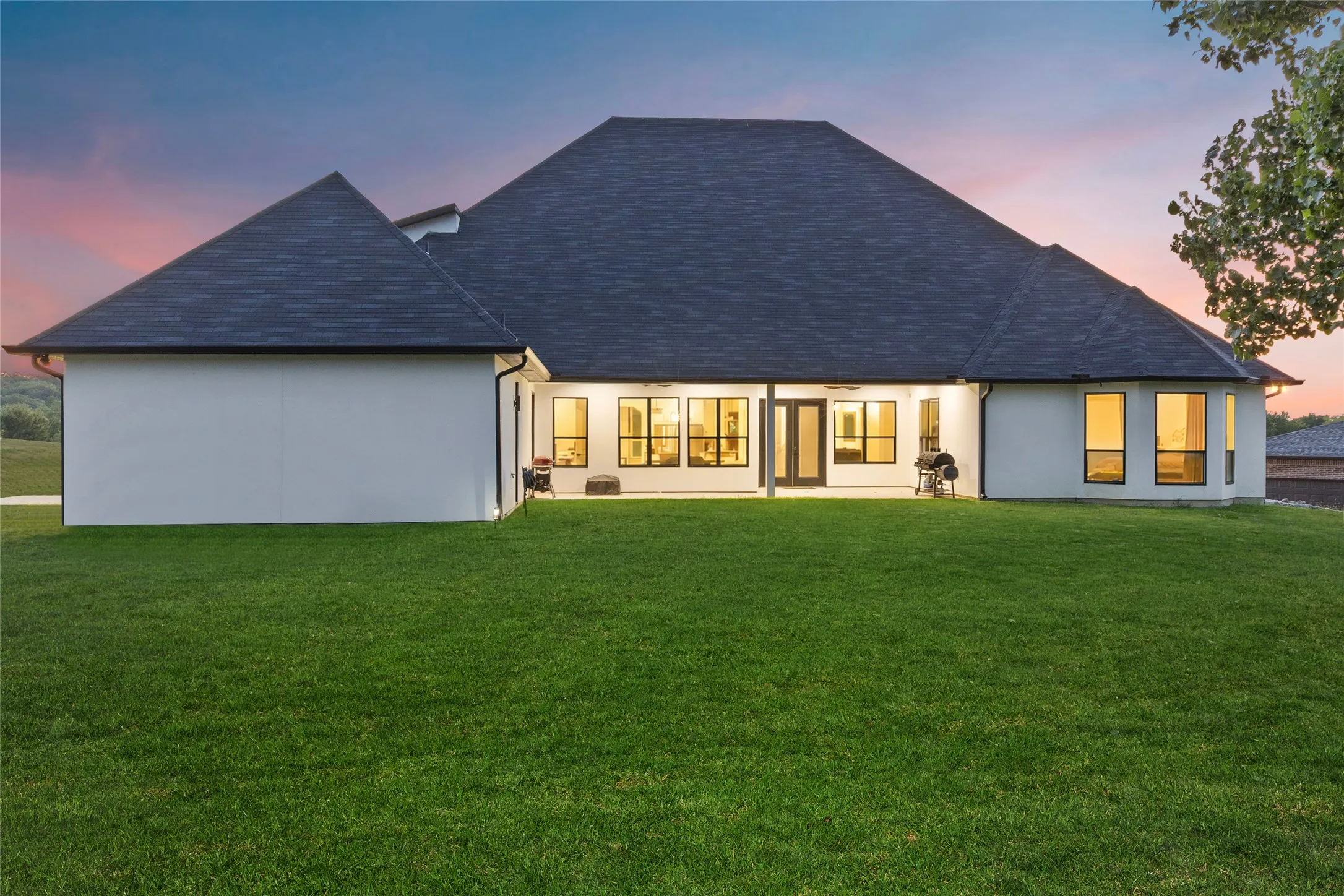 Expansive backyard featuring a large lawn, covered patio, multiple large windows, and a dark shingle roof