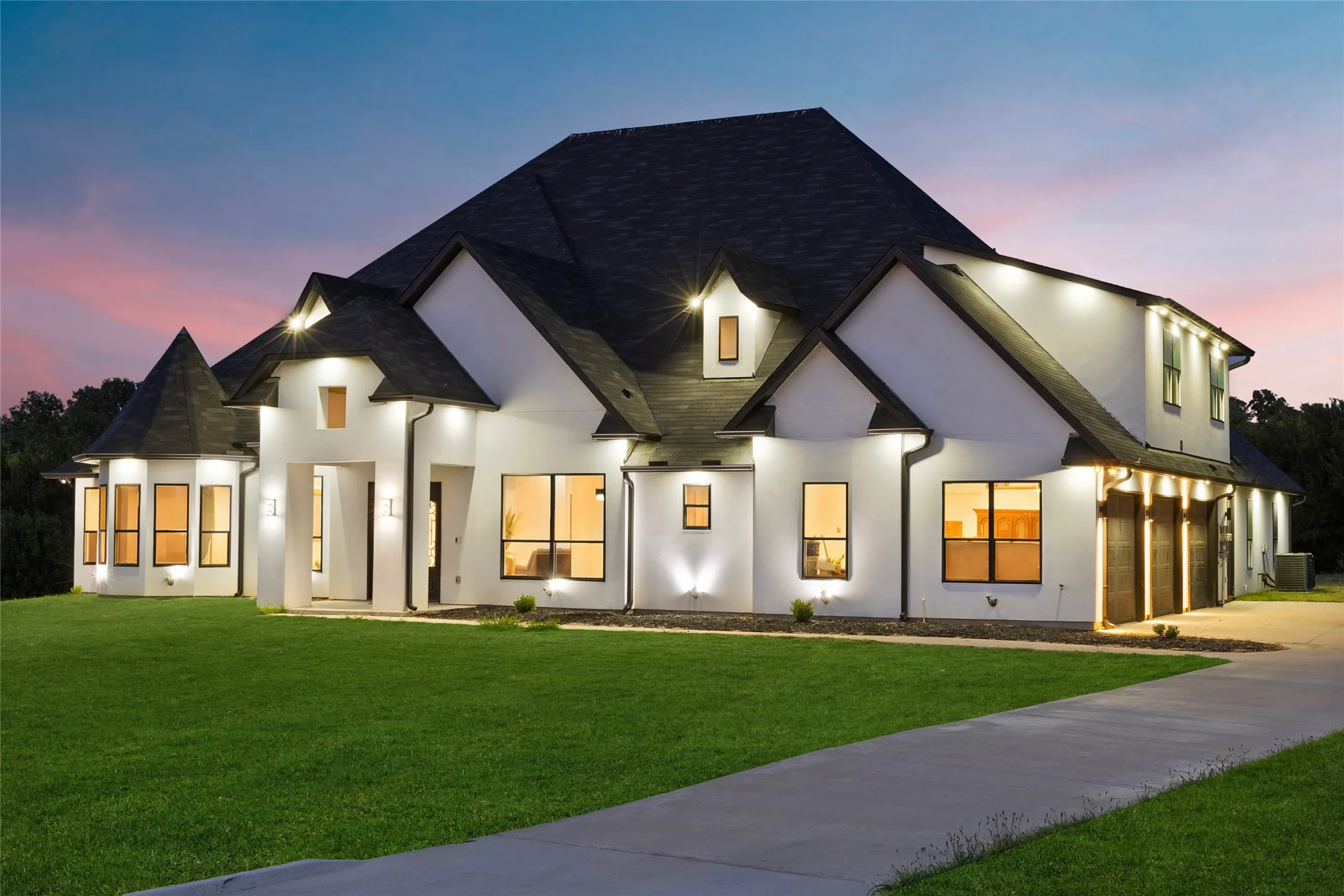 Contemporary exterior with white stucco finish, dark shingle roof, integrated exterior lighting, and a multi-car garage with wood-finish doors