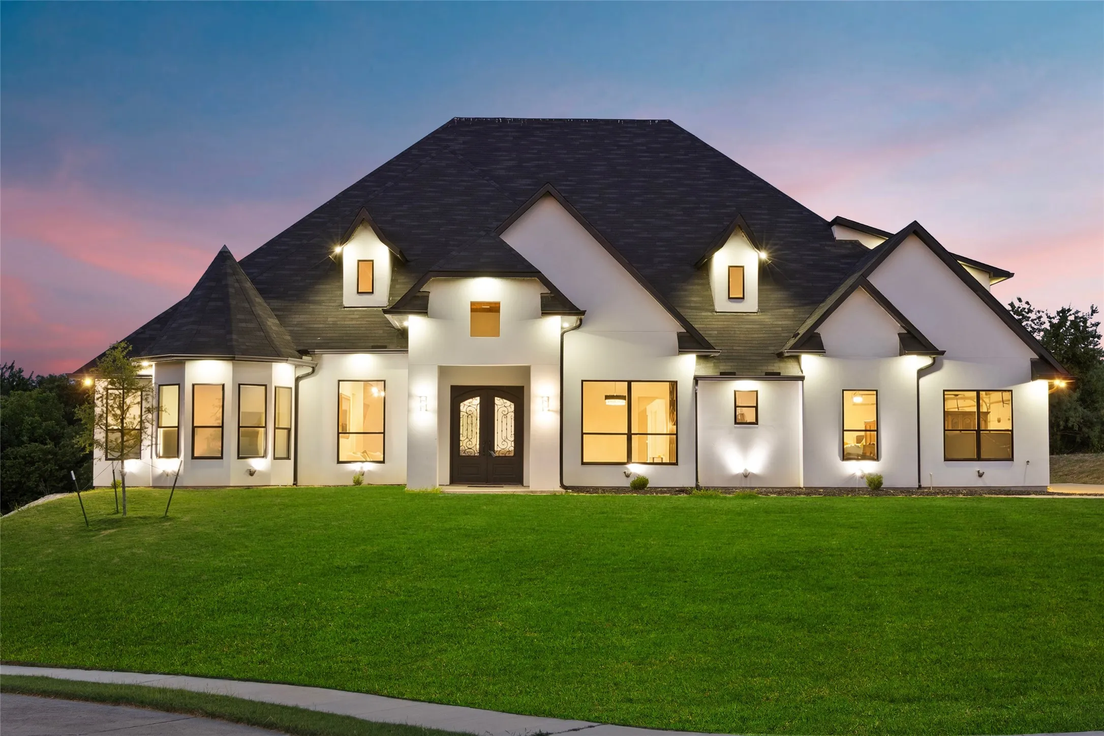 White stucco exterior featuring a dark asphalt shingle roof, twin dormer windows, and a prominent double-door entry