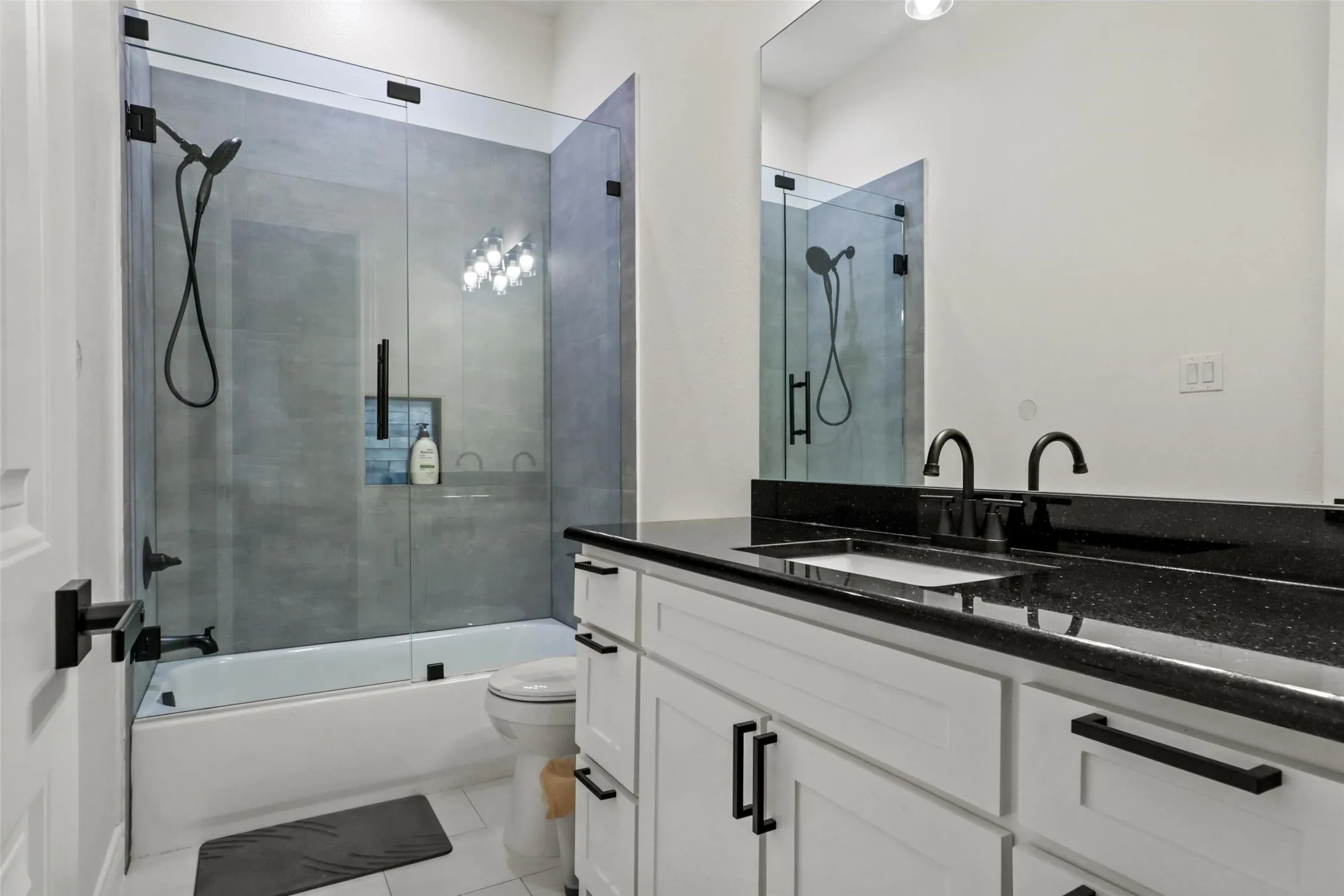 Dual vanity with dark stone countertop, white shaker-style cabinetry, and matte black fixtures