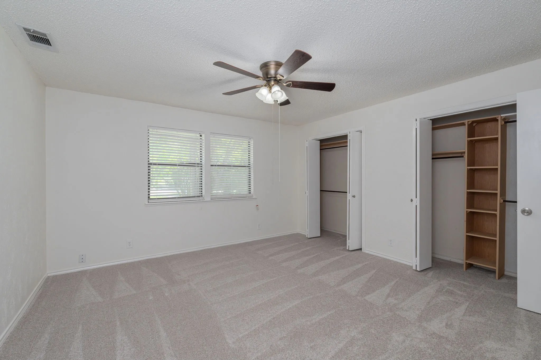 Spacious primary suite offers soft natural light, fresh neutral finishes, plush carpeting, and plenty of room for a king-size furniture arrangement.