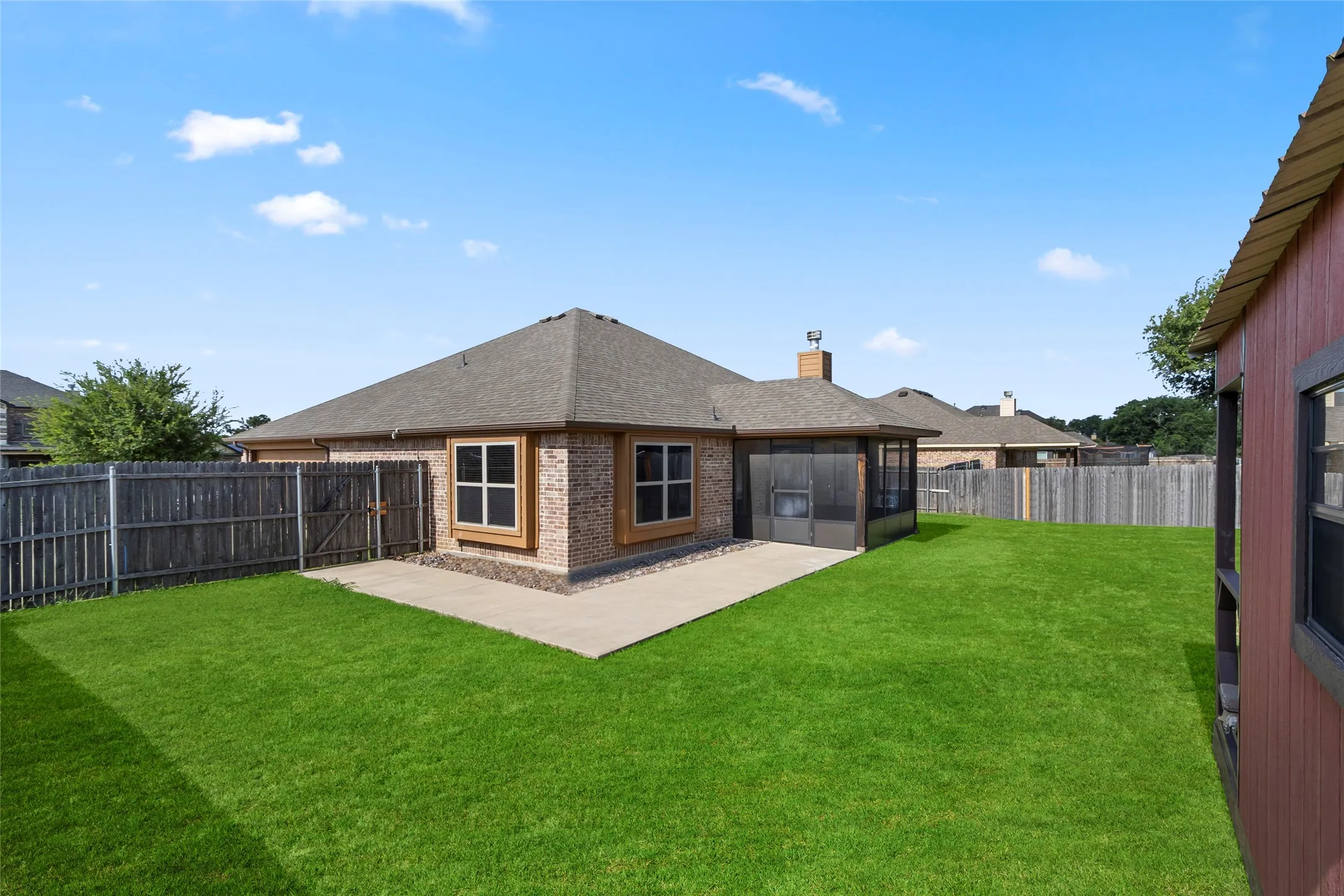 Expansive backyard featuring a manicured lawn, concrete patio, privacy fencing, brick exterior, and a screened-in porch