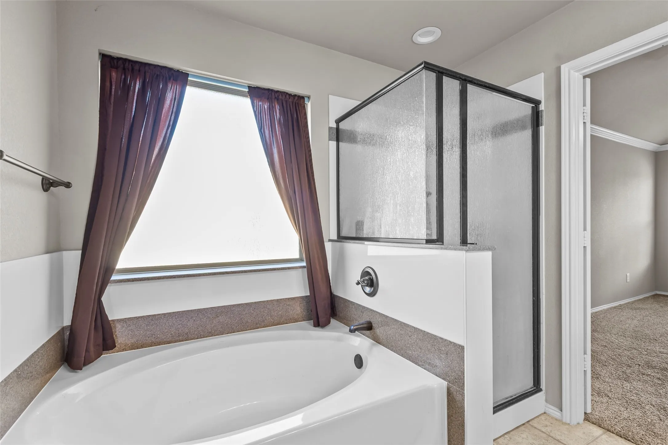 Soaking tub with a tiled surround, framed window, and an adjacent shower enclosure featuring clear glass panels and a black frame