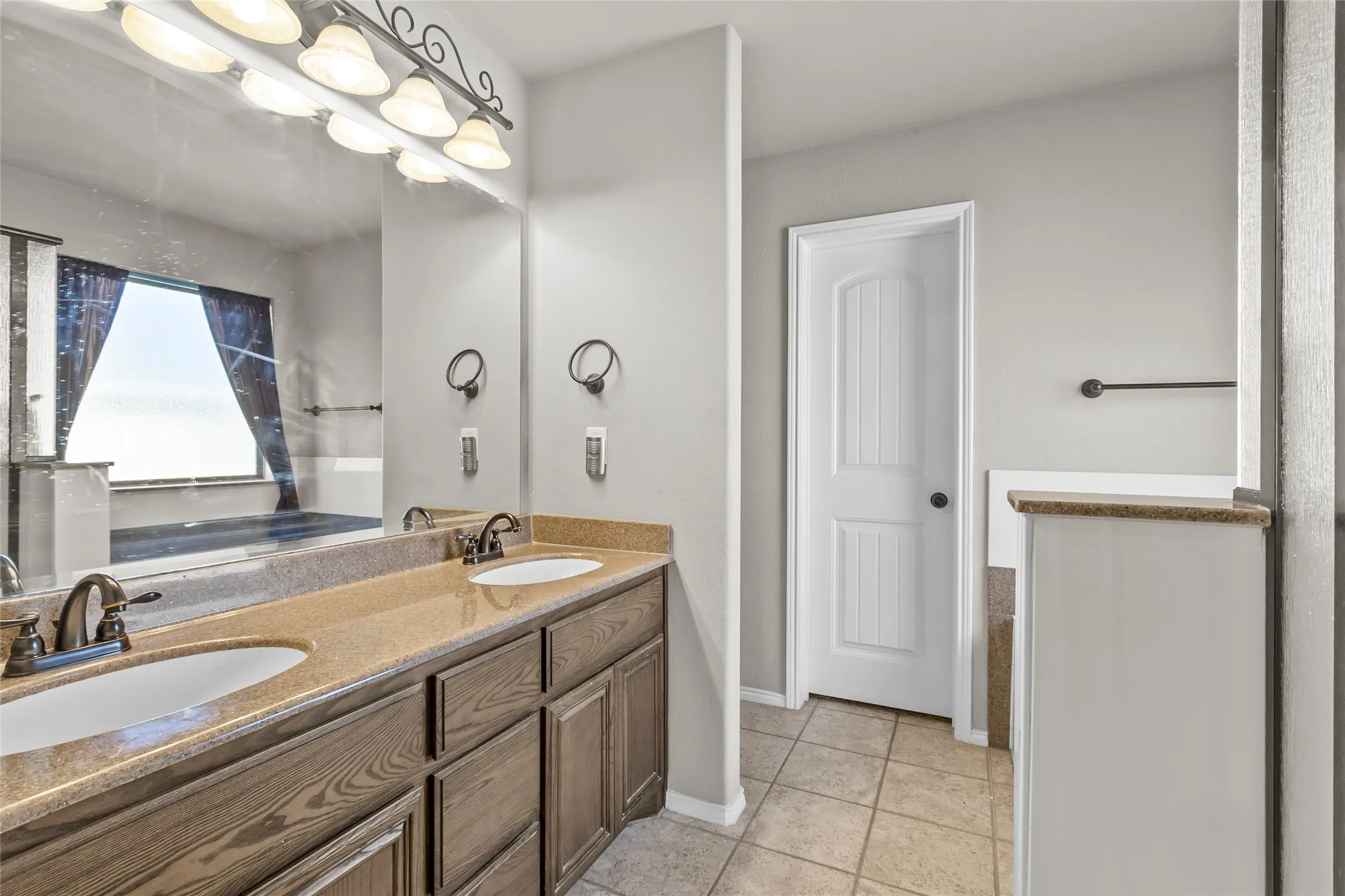 Dual vanity with wood-finish cabinetry, light-toned countertops, and bronze-finish fixtures