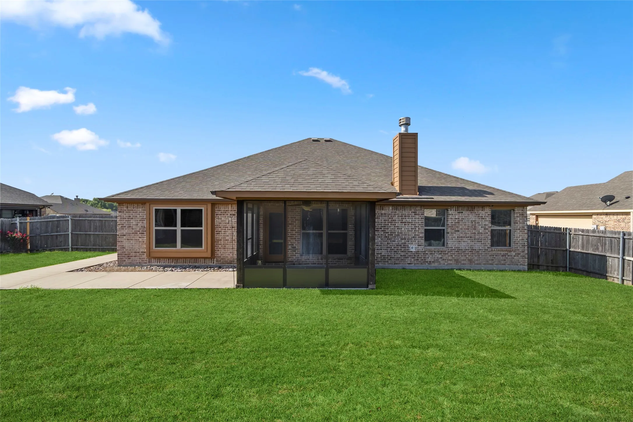 Spacious backyard featuring a large screened-in porch, concrete patio, and extensive green lawn