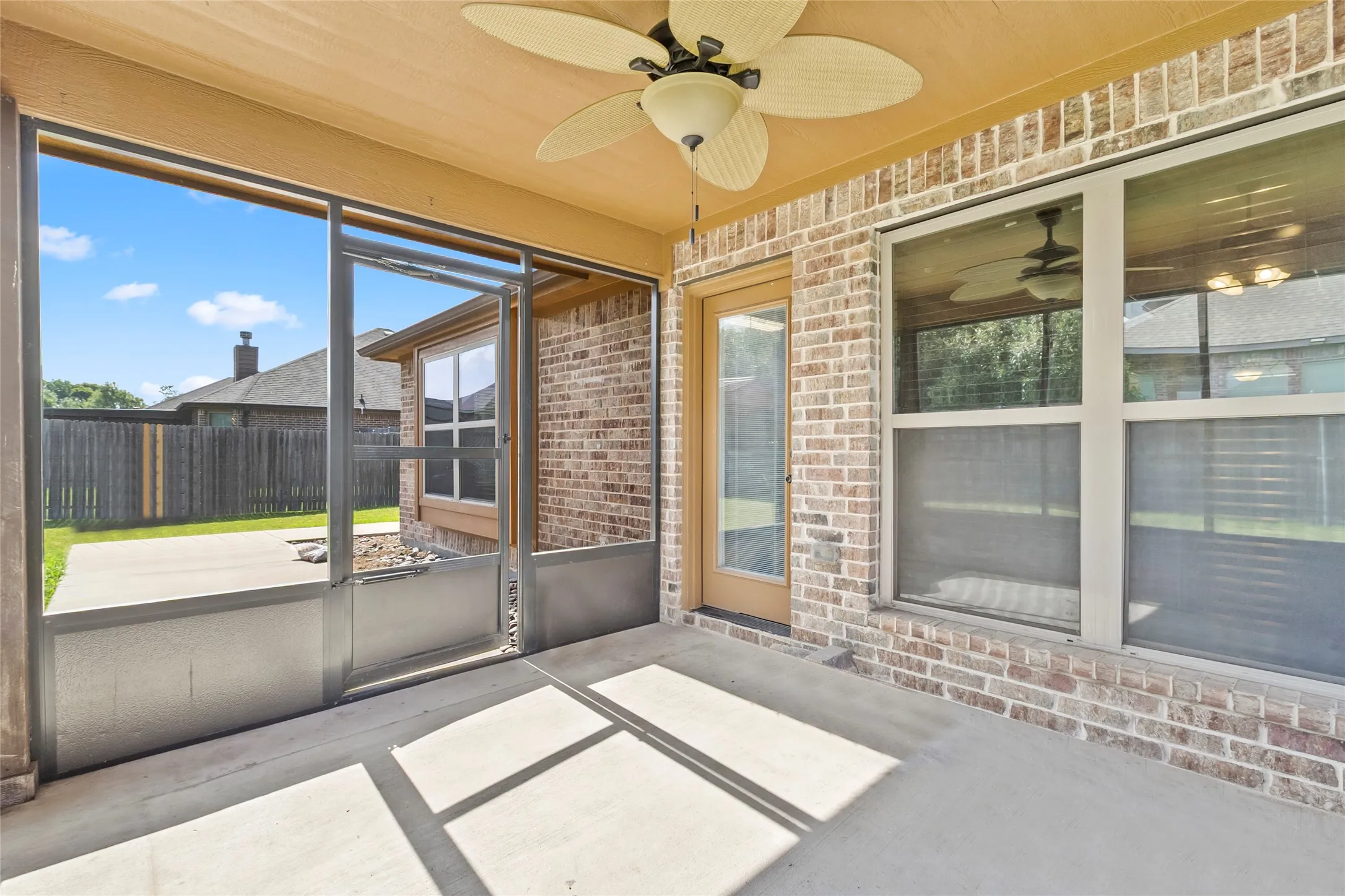 Screened patio featuring a concrete floor, ceiling fan, brick exterior, and direct access to the backyard