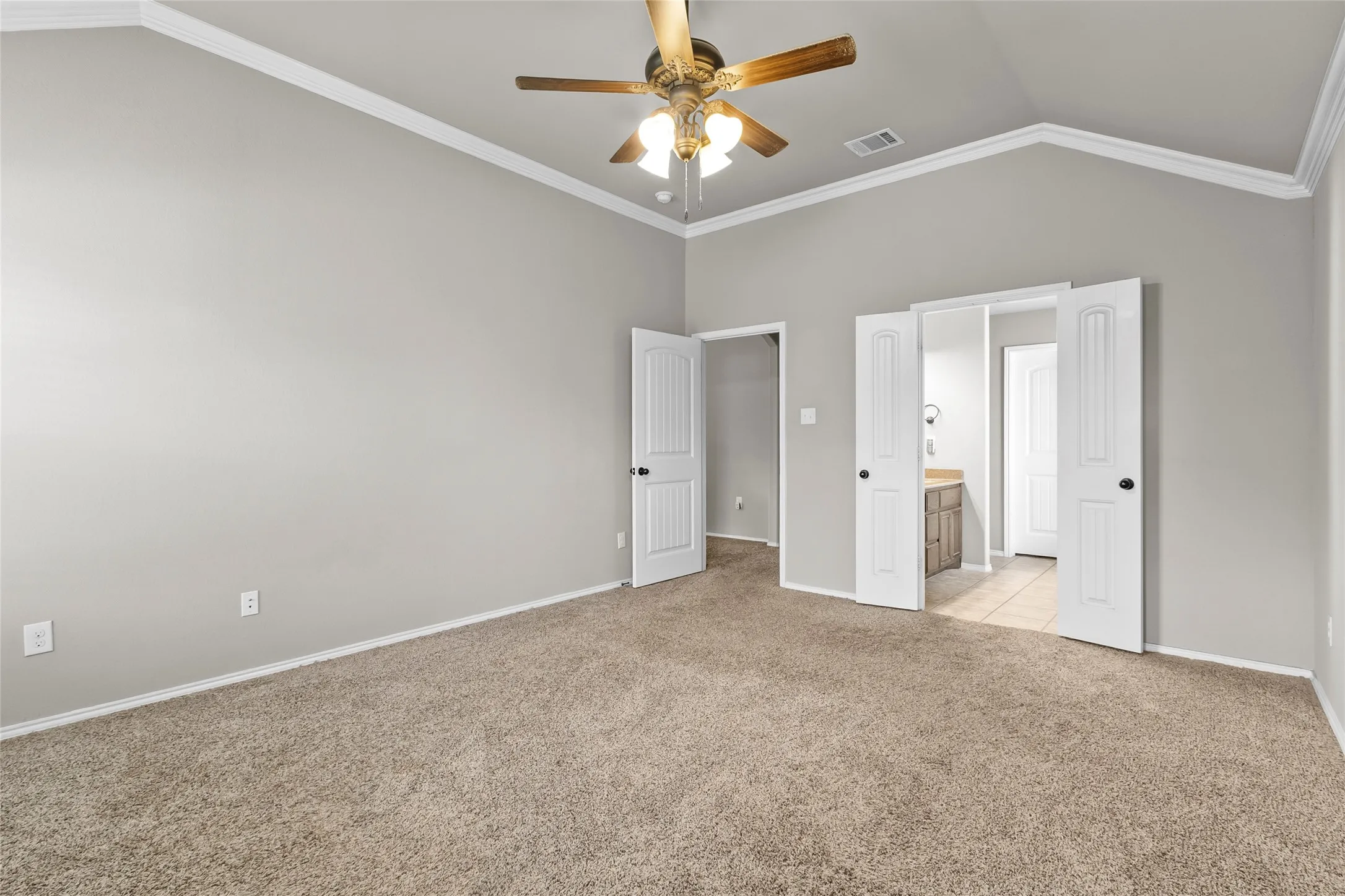 Spacious room featuring vaulted ceilings, crown molding, a ceiling fan, and carpeted flooring
