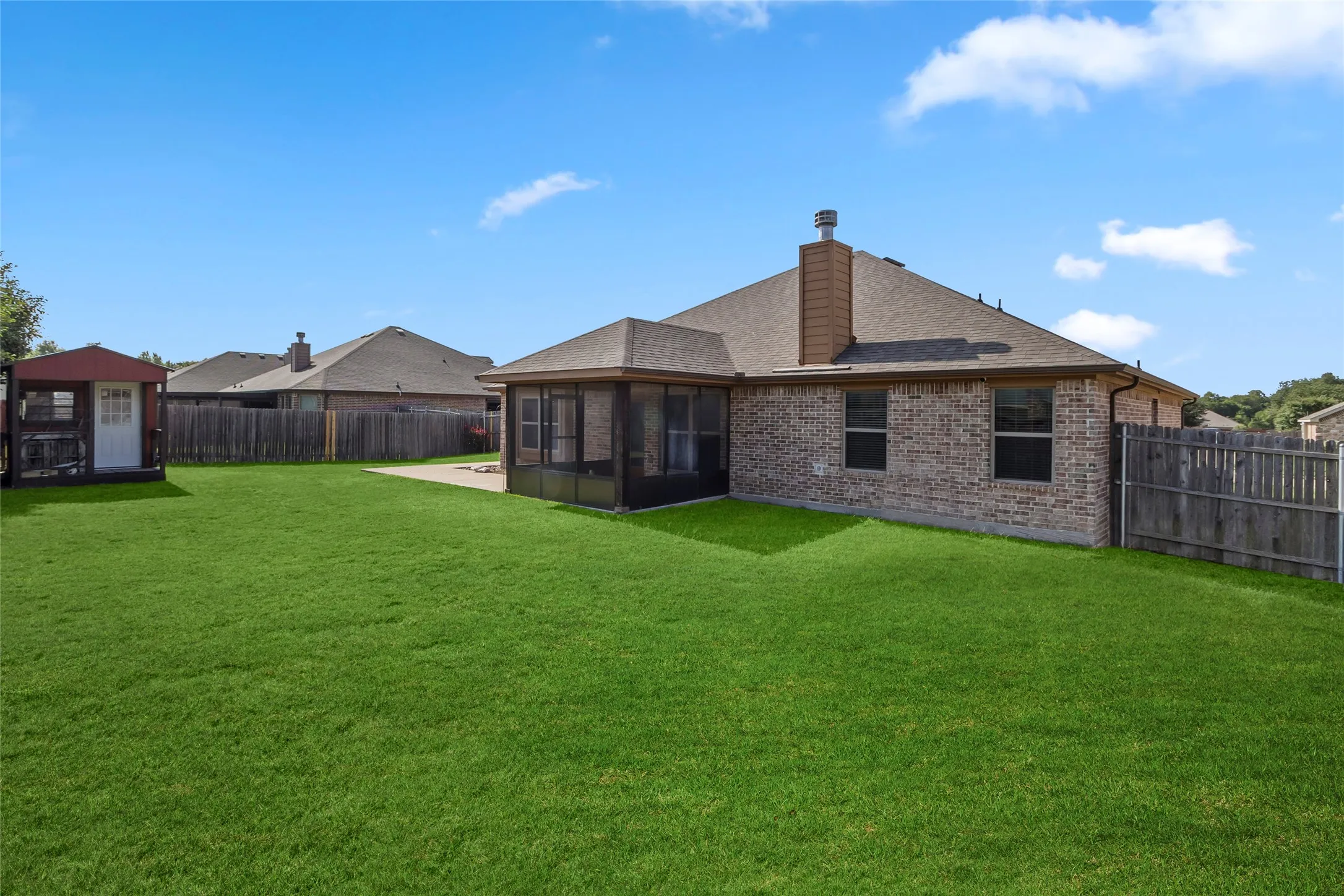 Expansive backyard featuring a lush lawn, brick exterior, screened patio, concrete patio, and a detached storage shed
